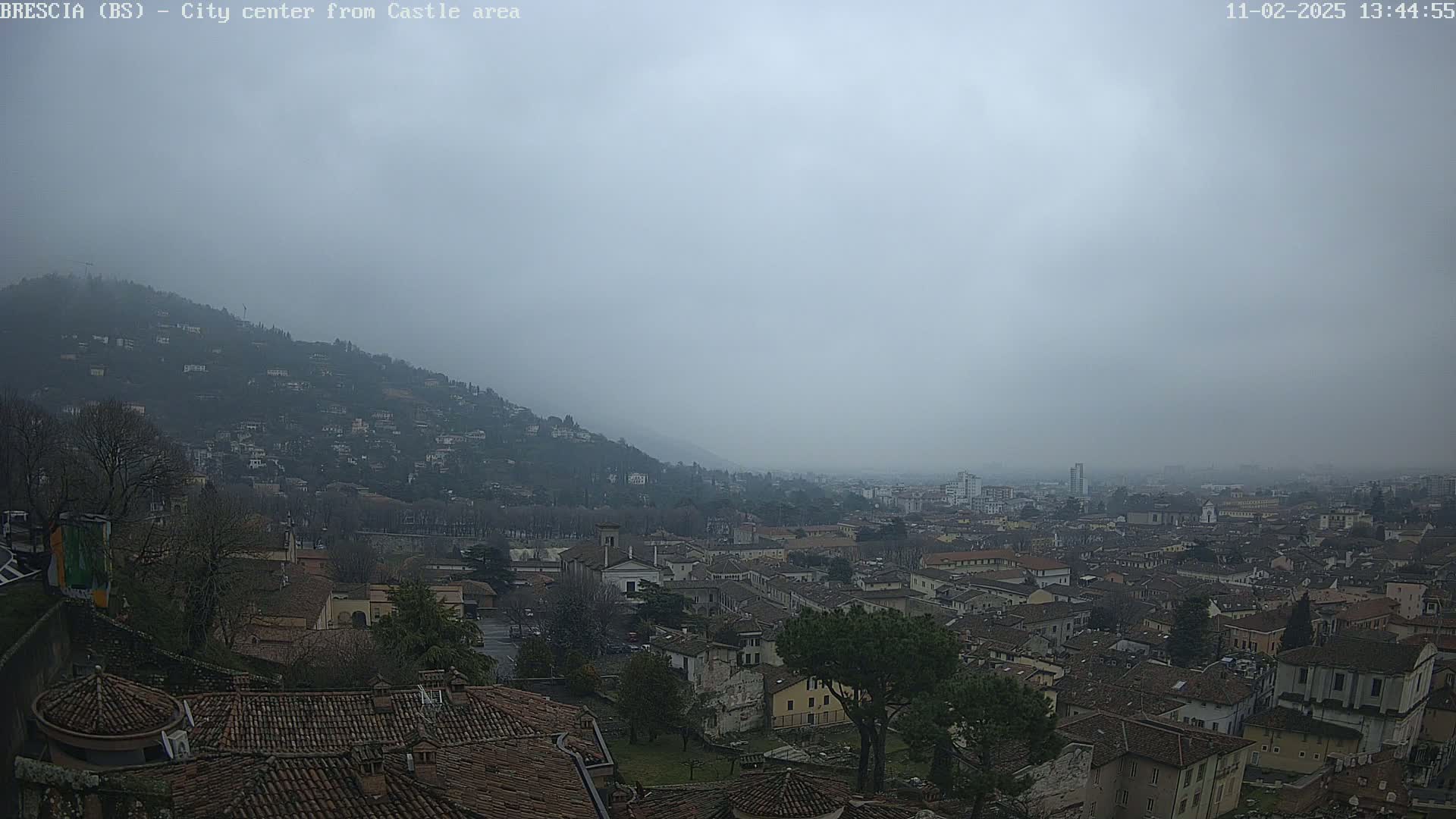 A hazy, overcast view of a city nestled in a valley, with a hill covered in buildings in the background.