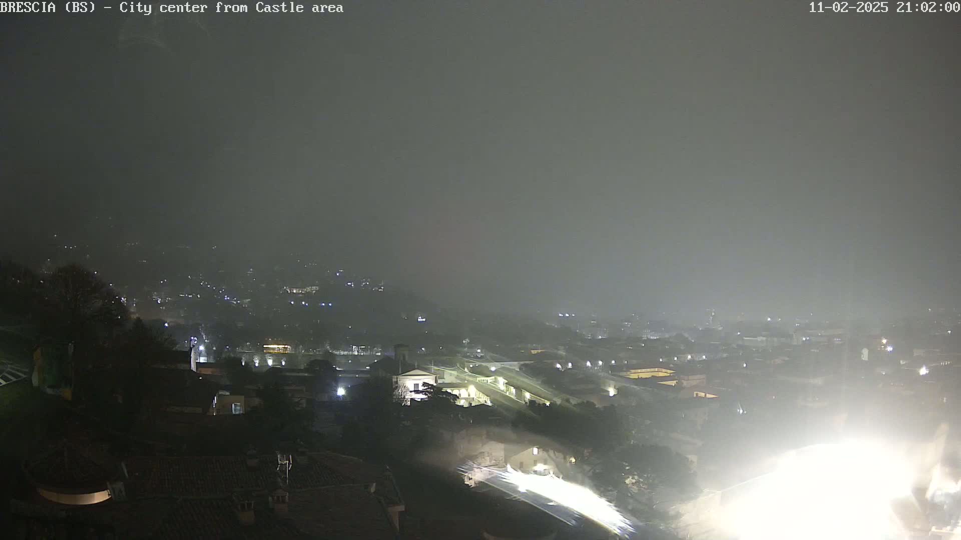 A nighttime, hazy view of a city spread across hills, with lights illuminating buildings and streets.