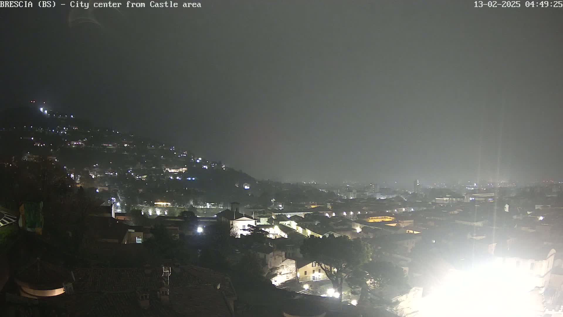 A nighttime view of a city sprawling across a hill, shrouded in hazy weather conditions.