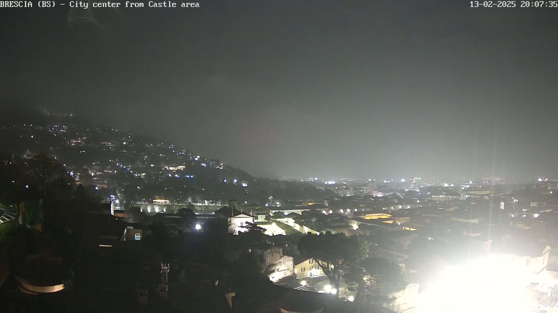 A nighttime view of a city sprawling across a hillside under a hazy, dark sky.