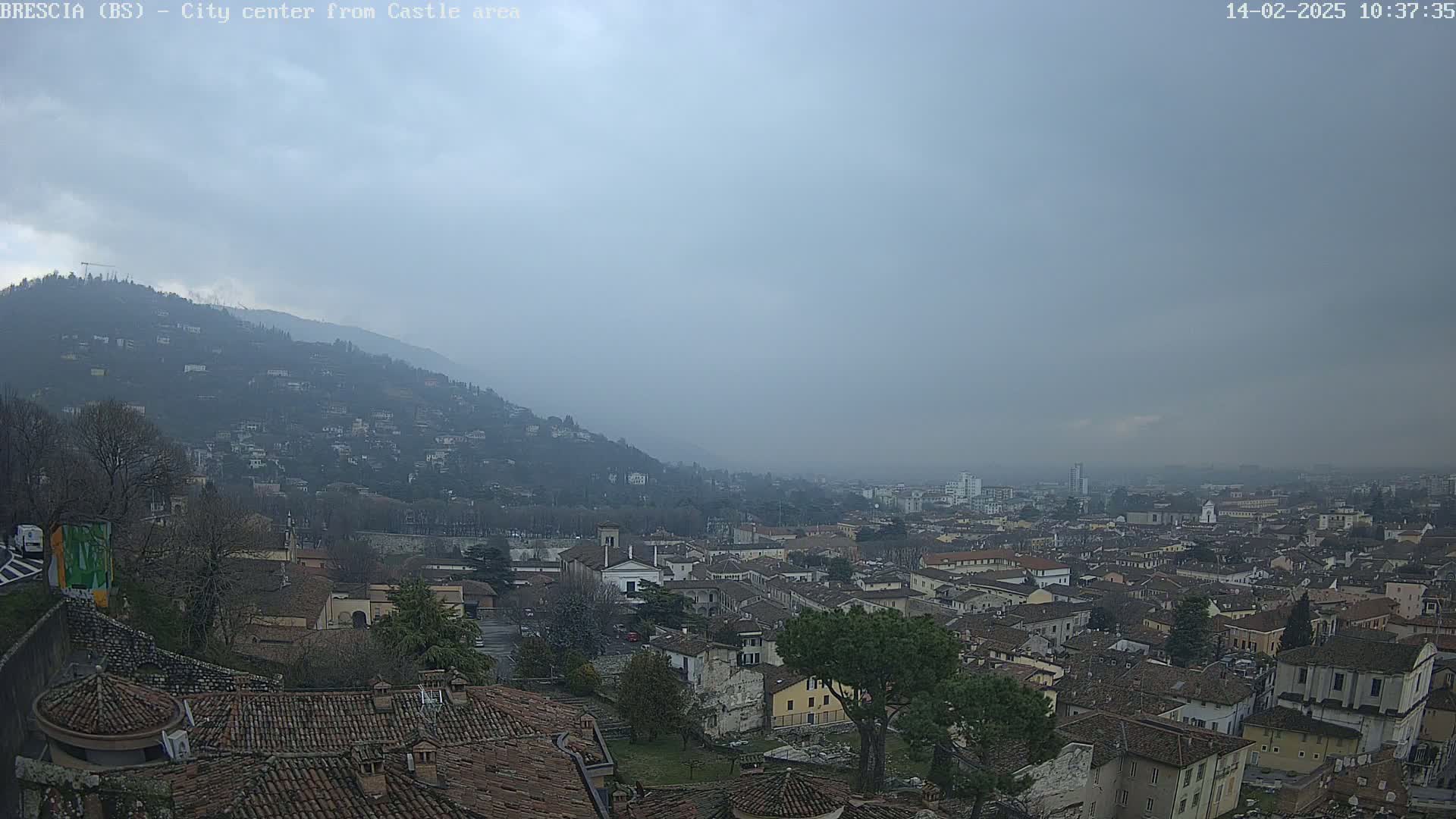 A hazy, overcast day reveals a sprawling city nestled at the base of a hill, with numerous buildings and terracotta rooftops stretching into the distance.