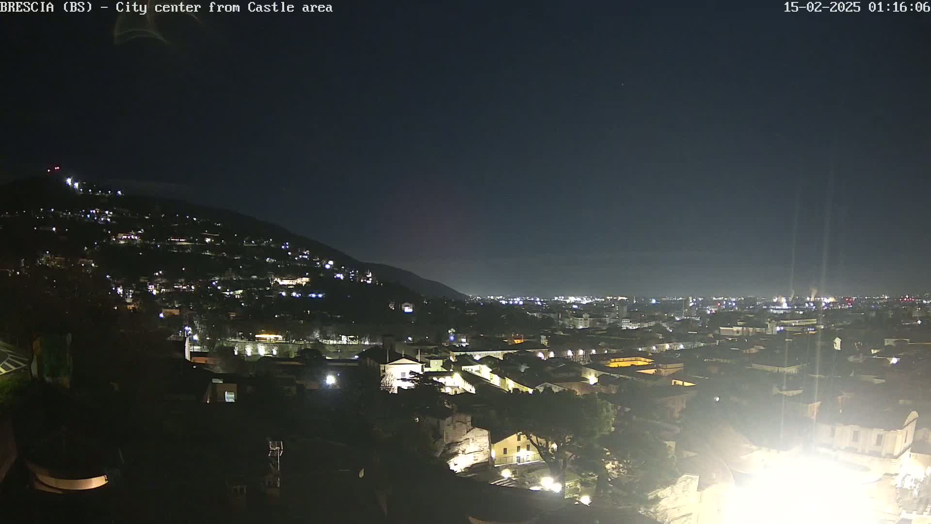 A nighttime view of a city nestled against a hill, illuminated by scattered lights under a clear, dark sky.
