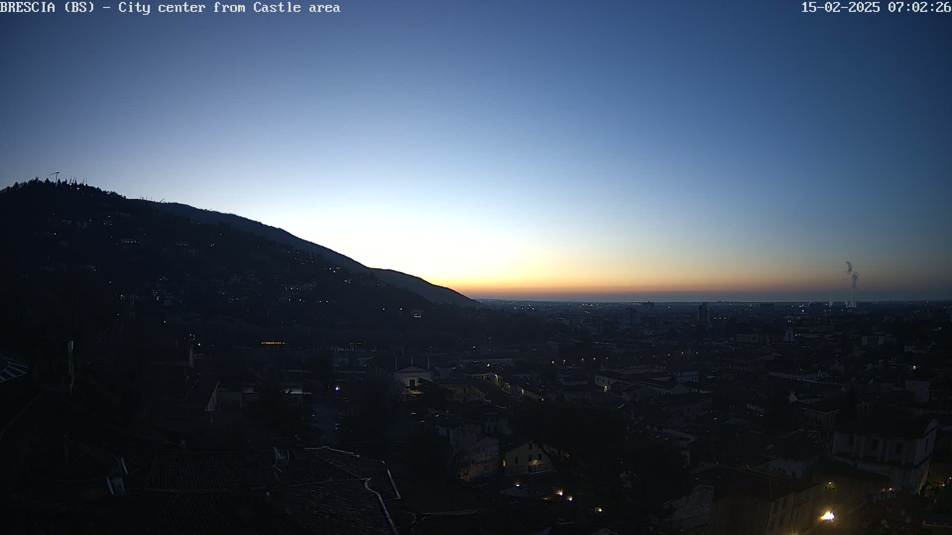 A city at sunrise is viewed from a hilltop, with a clear, twilight sky.