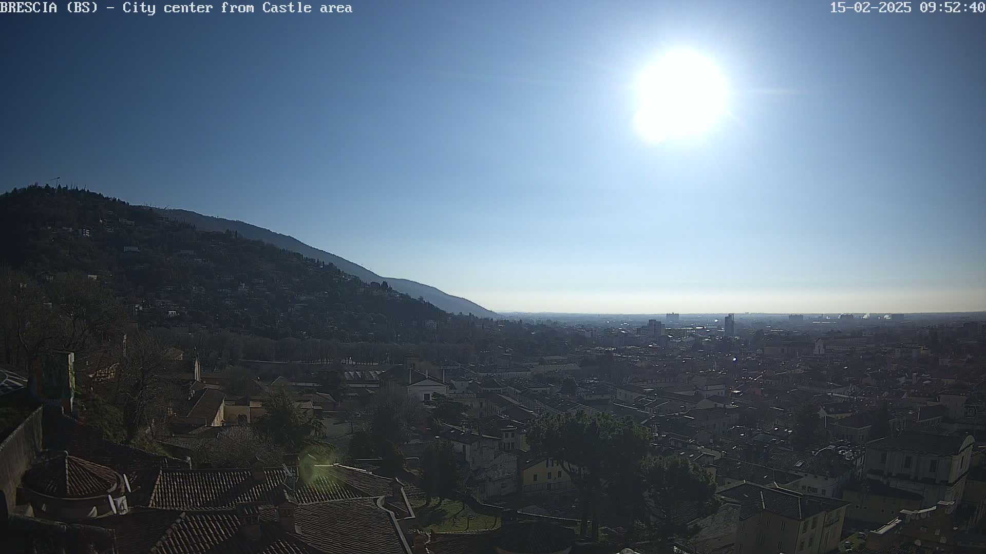 A sunny day reveals a sprawling city nestled below a hill, viewed from a high vantage point.