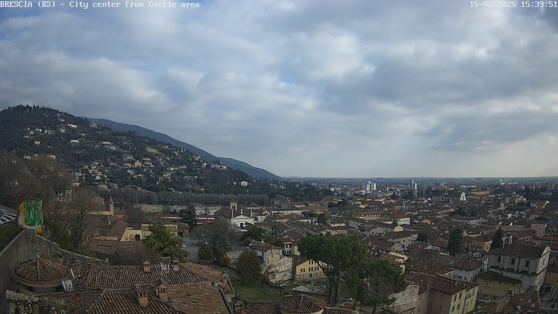 A sprawling city, nestled beneath a hill dotted with buildings, stretches out under a cloudy sky.