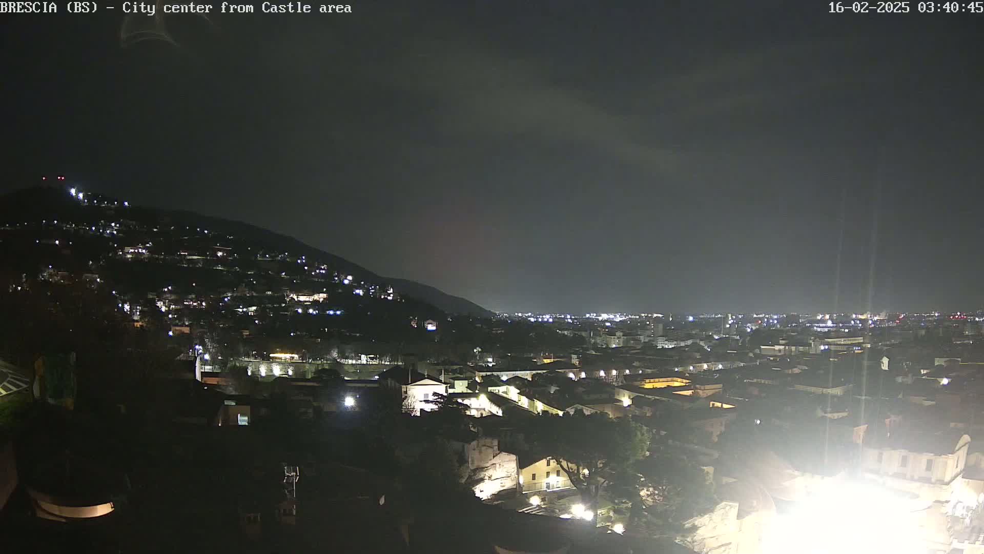 A nighttime view of a city nestled into a hillside, illuminated by scattered lights under a dark, clear sky.