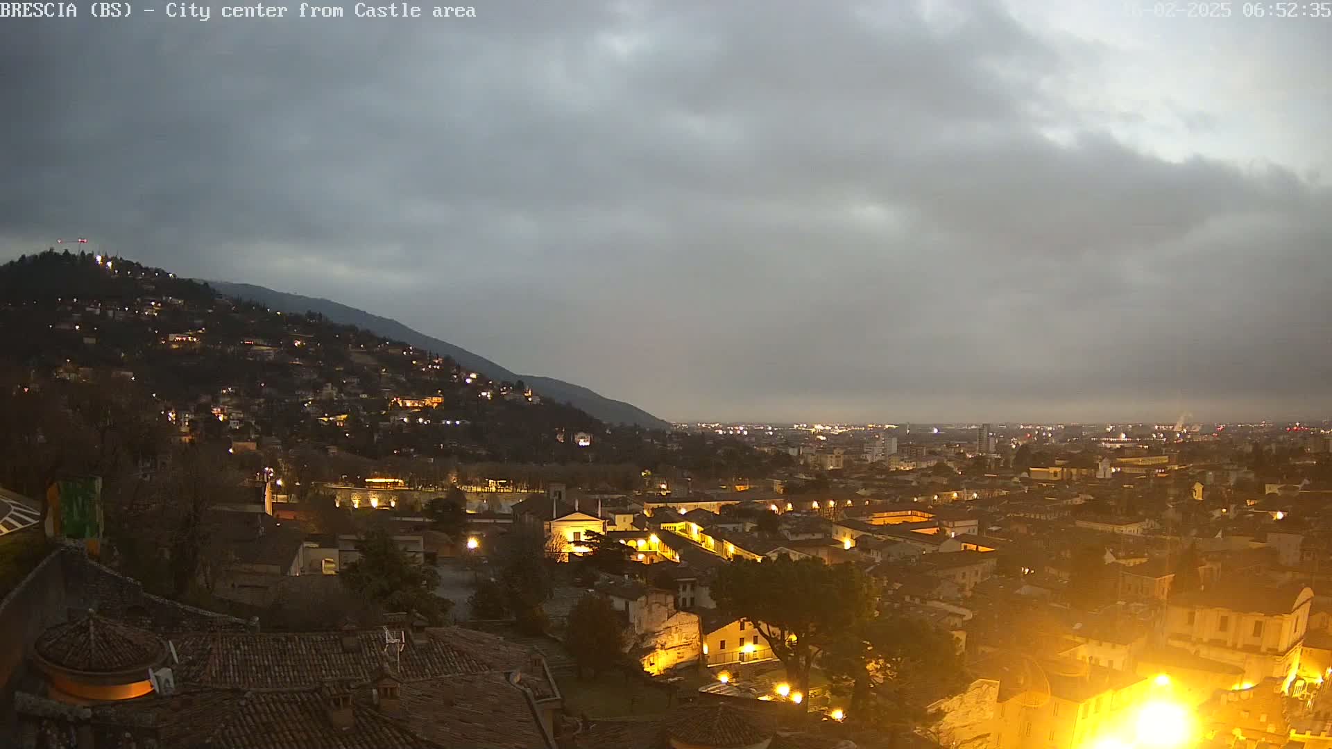A nighttime view of a city nestled against a hill, under a cloudy sky.
