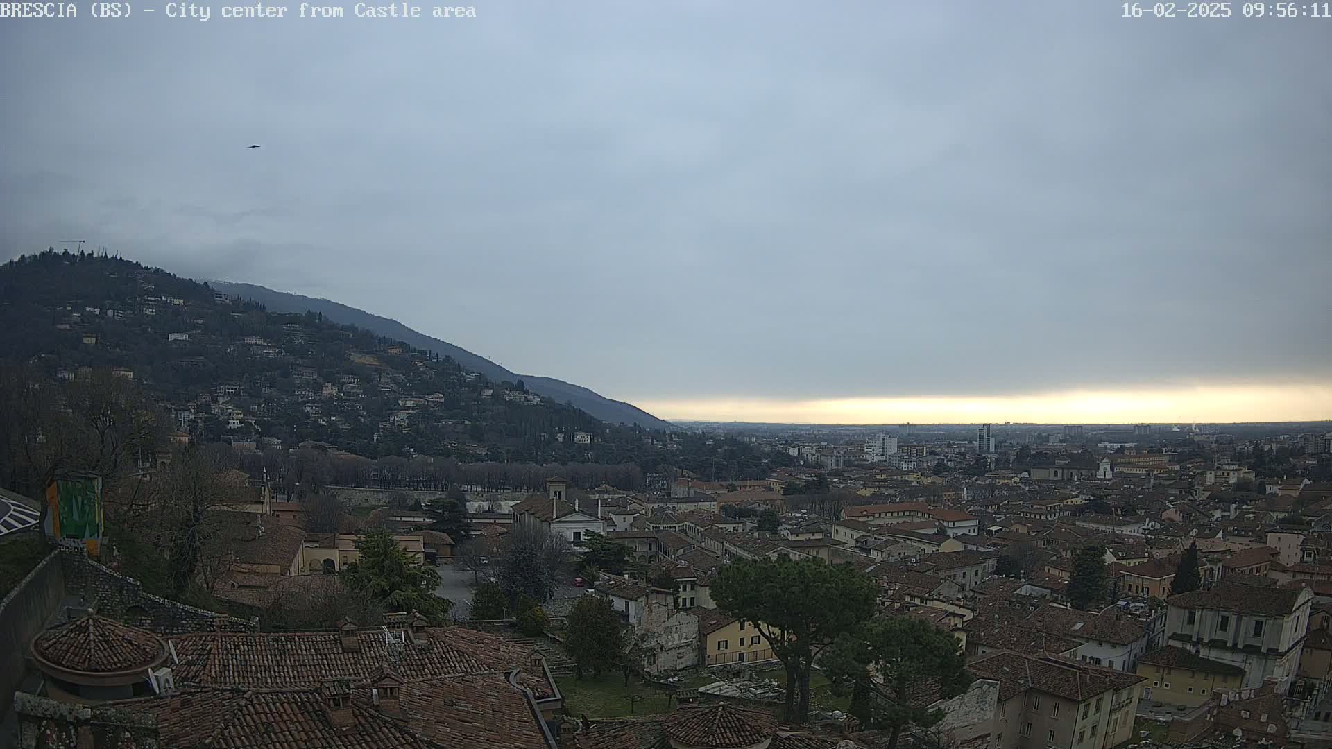 A sprawling city nestled at the foot of a mountain under a cloudy, overcast sky.