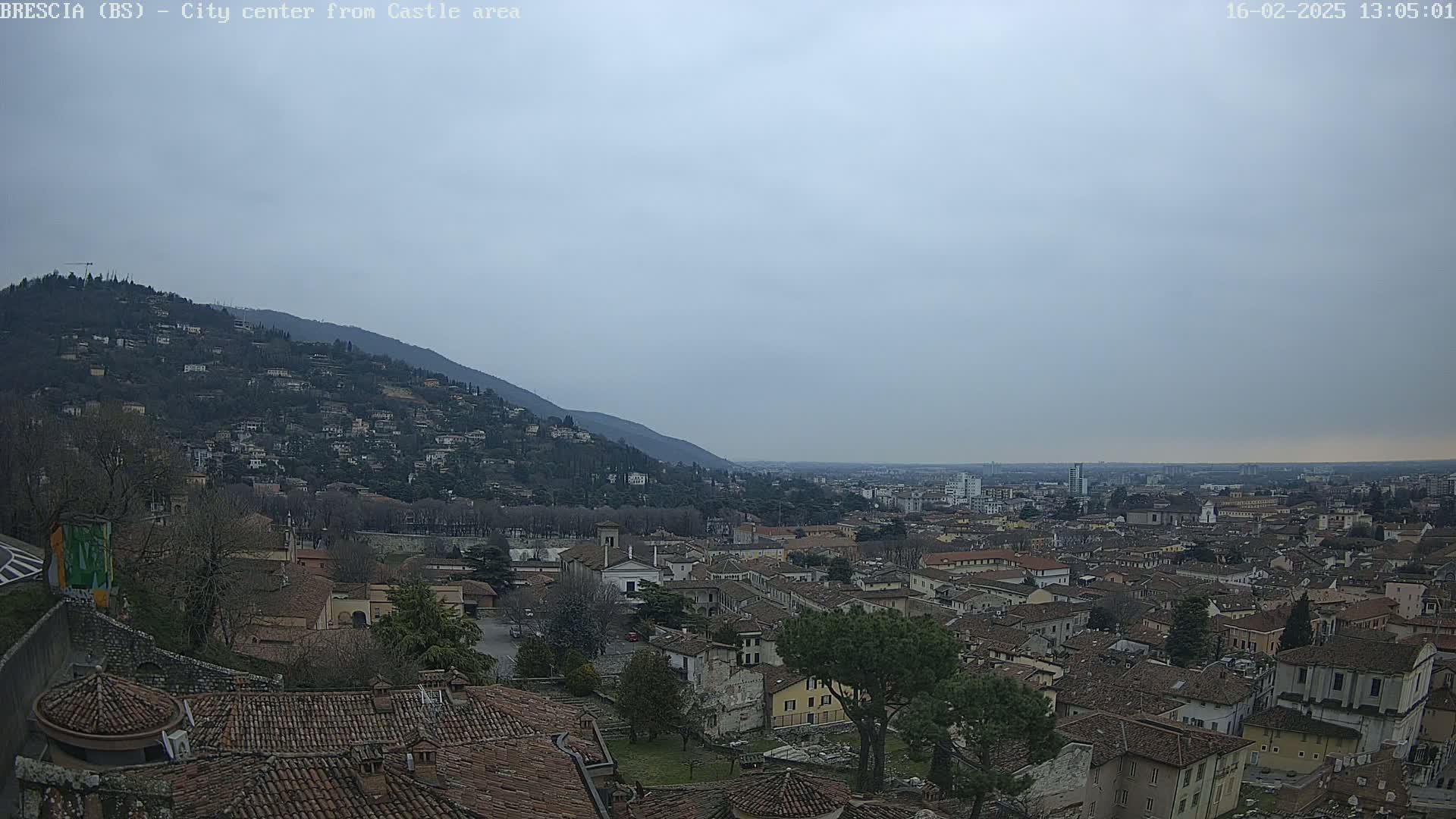 A sprawling city nestled in a valley beneath a hill, viewed on an overcast day.