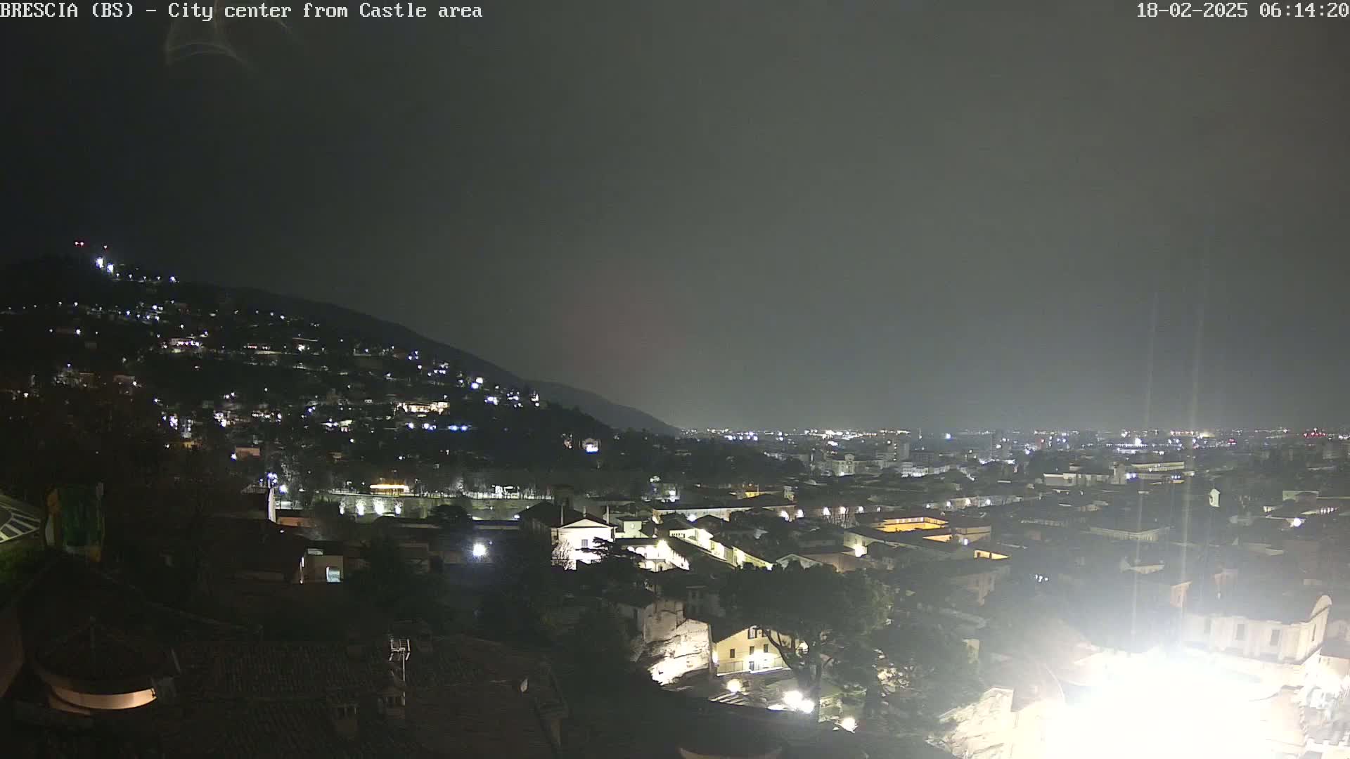 A nighttime view of a city nestled against a hill, under a dark, overcast sky.