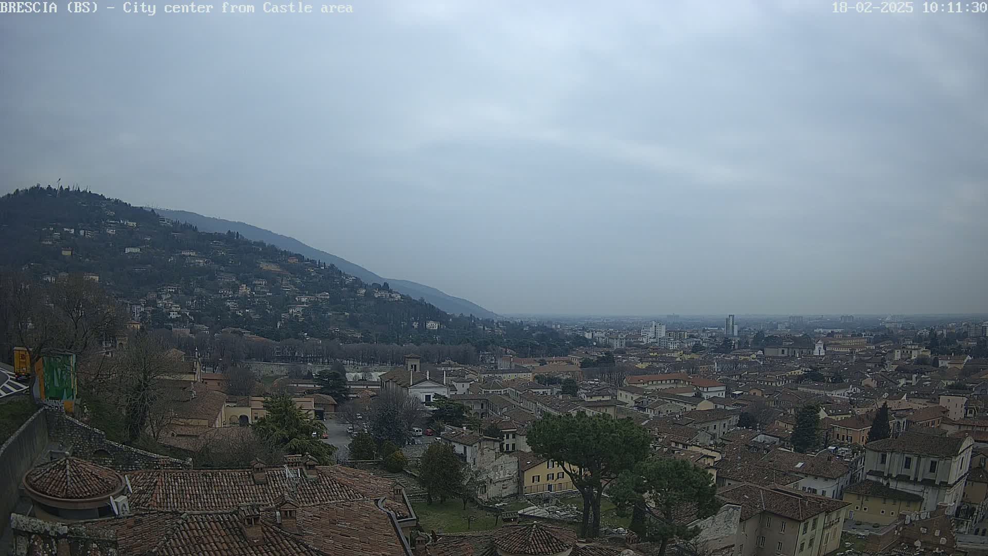 A view from a hilltop shows a city sprawling across a valley under a cloudy sky.
