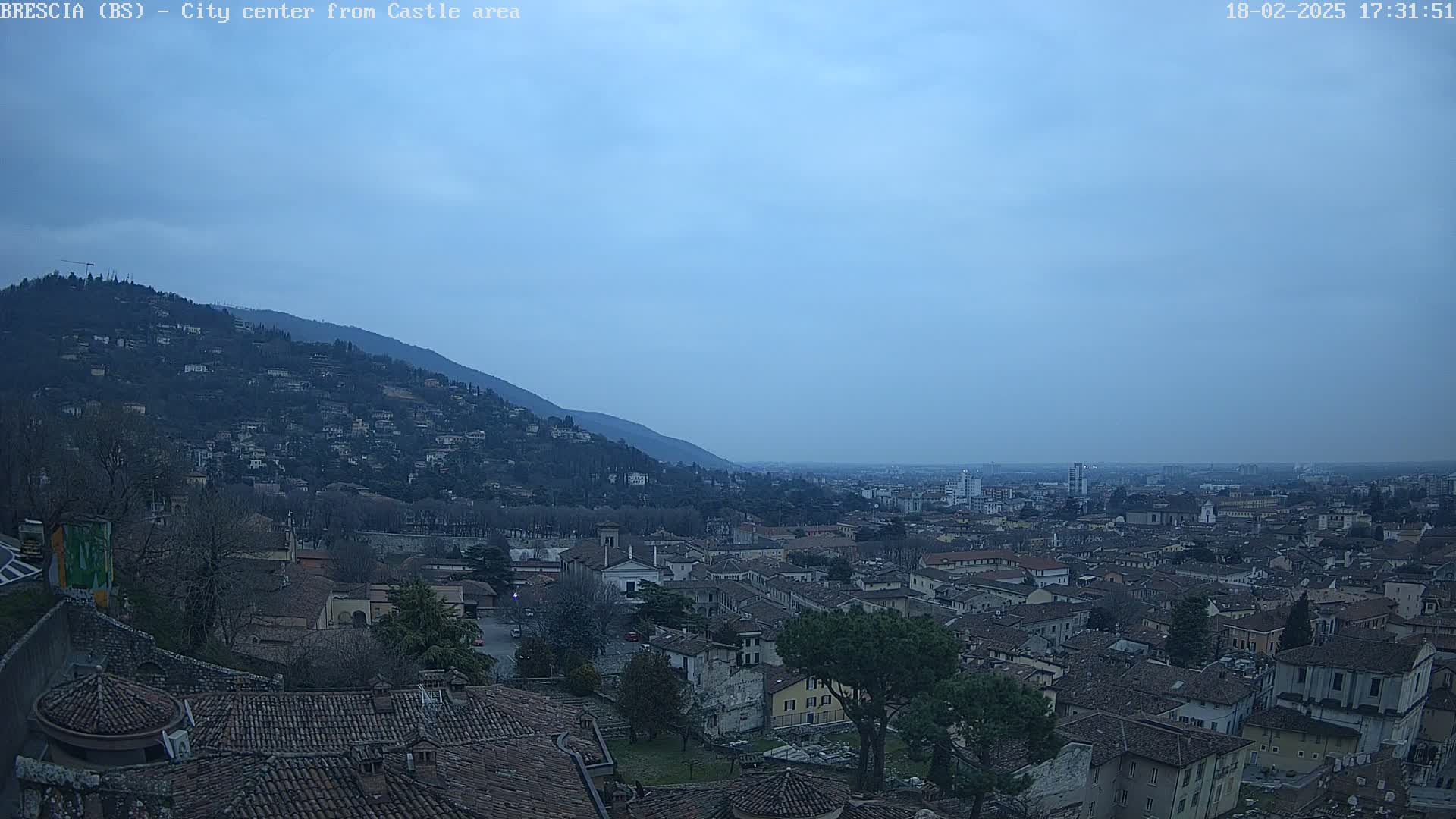 A city nestled in a valley between hills under a dusky blue sky.