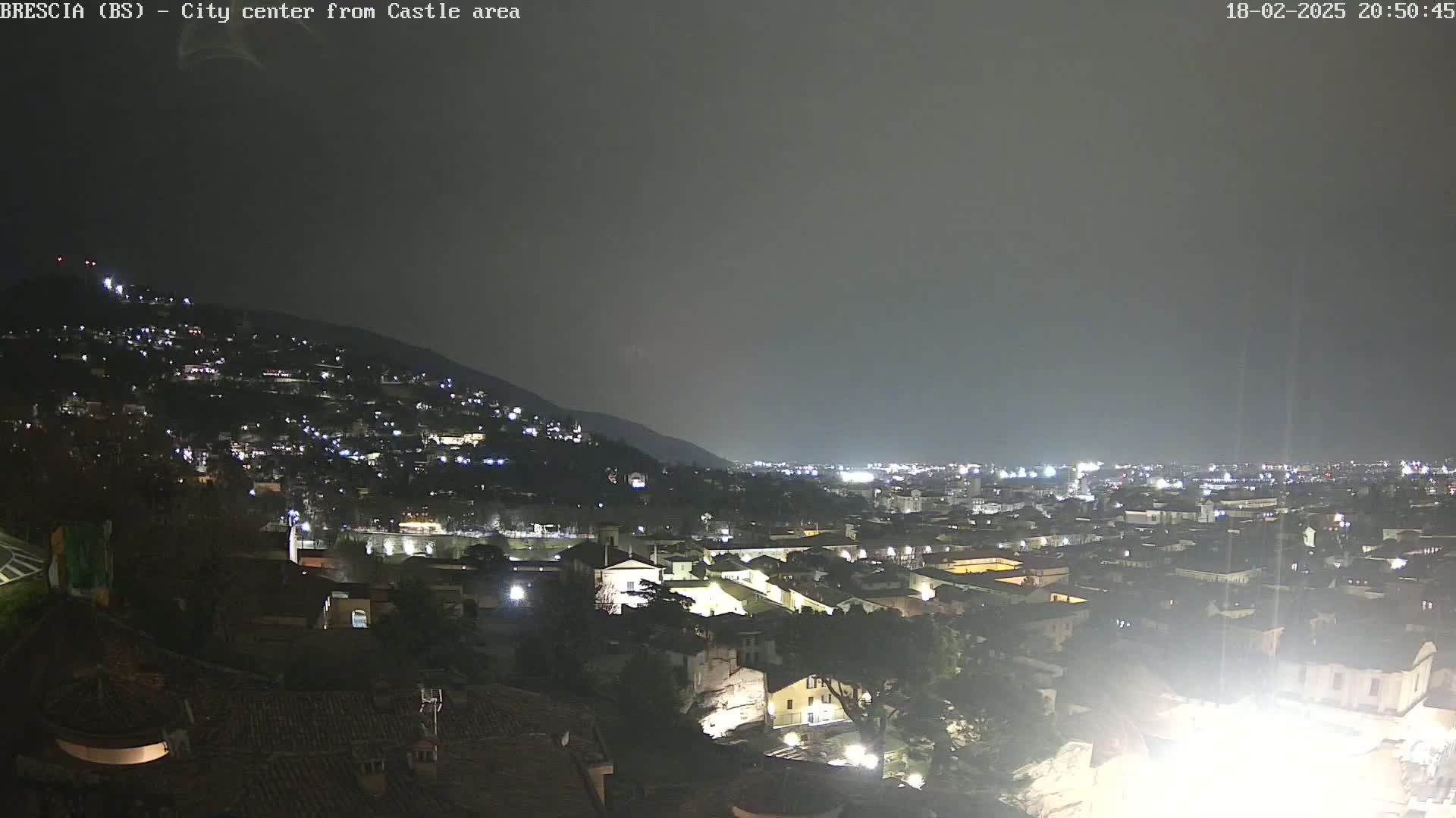 A nighttime view of a city nestled against a hillside, under a dark, overcast sky.
