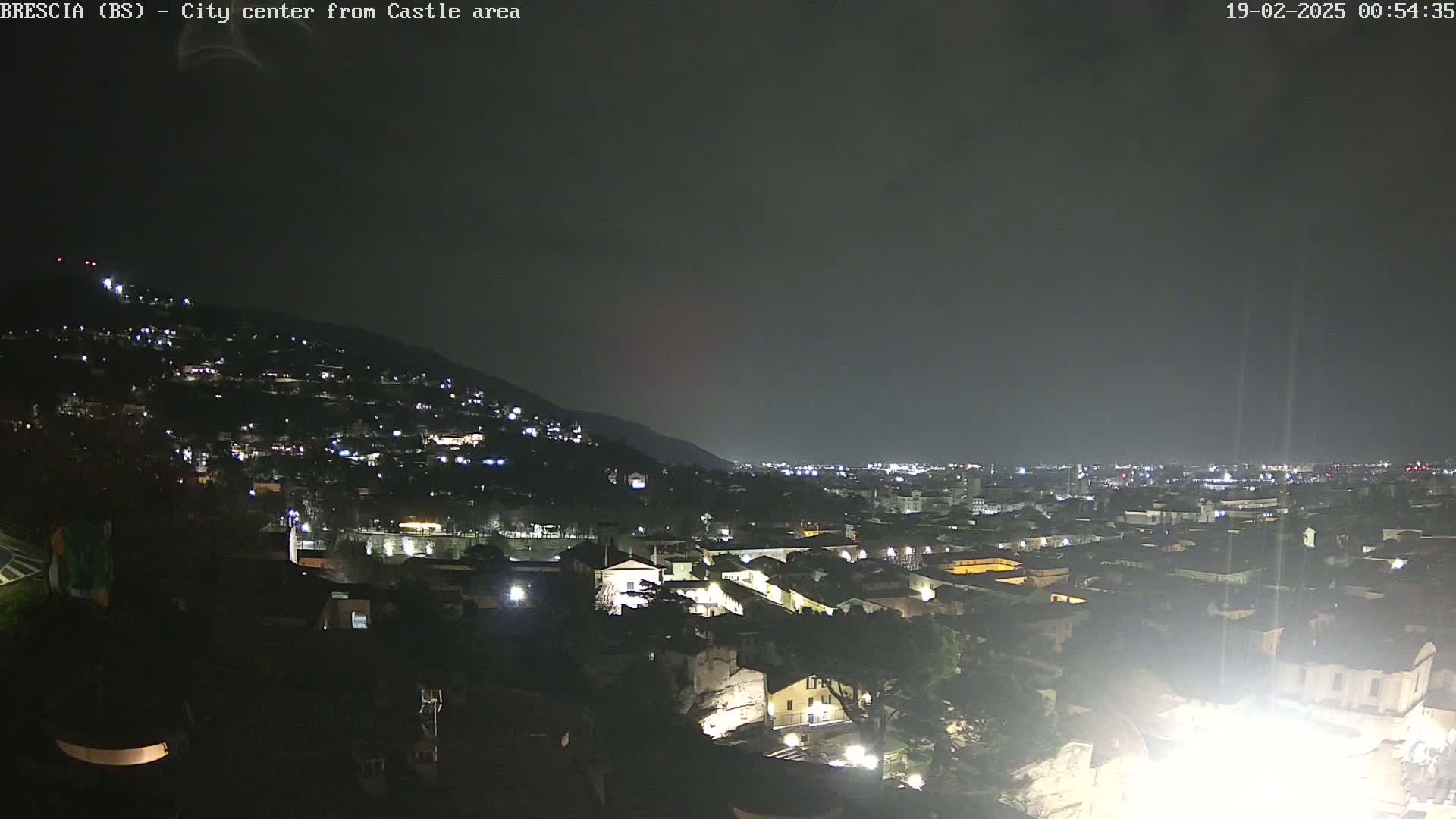 A nighttime view of a city nestled against a hill, under a dark, overcast sky.