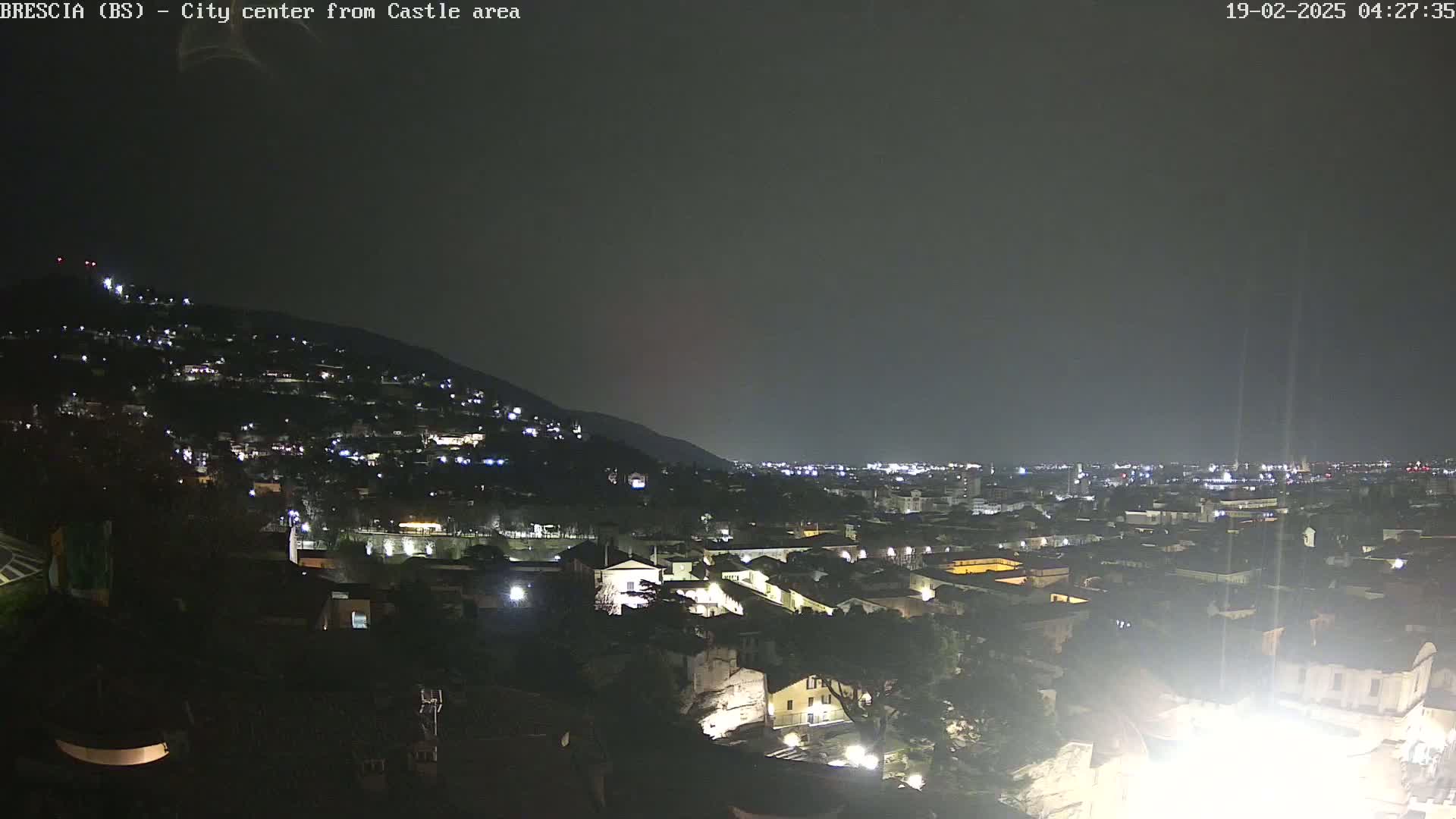 A nighttime view of a city nestled against a hillside, illuminated by numerous lights under a dark sky.