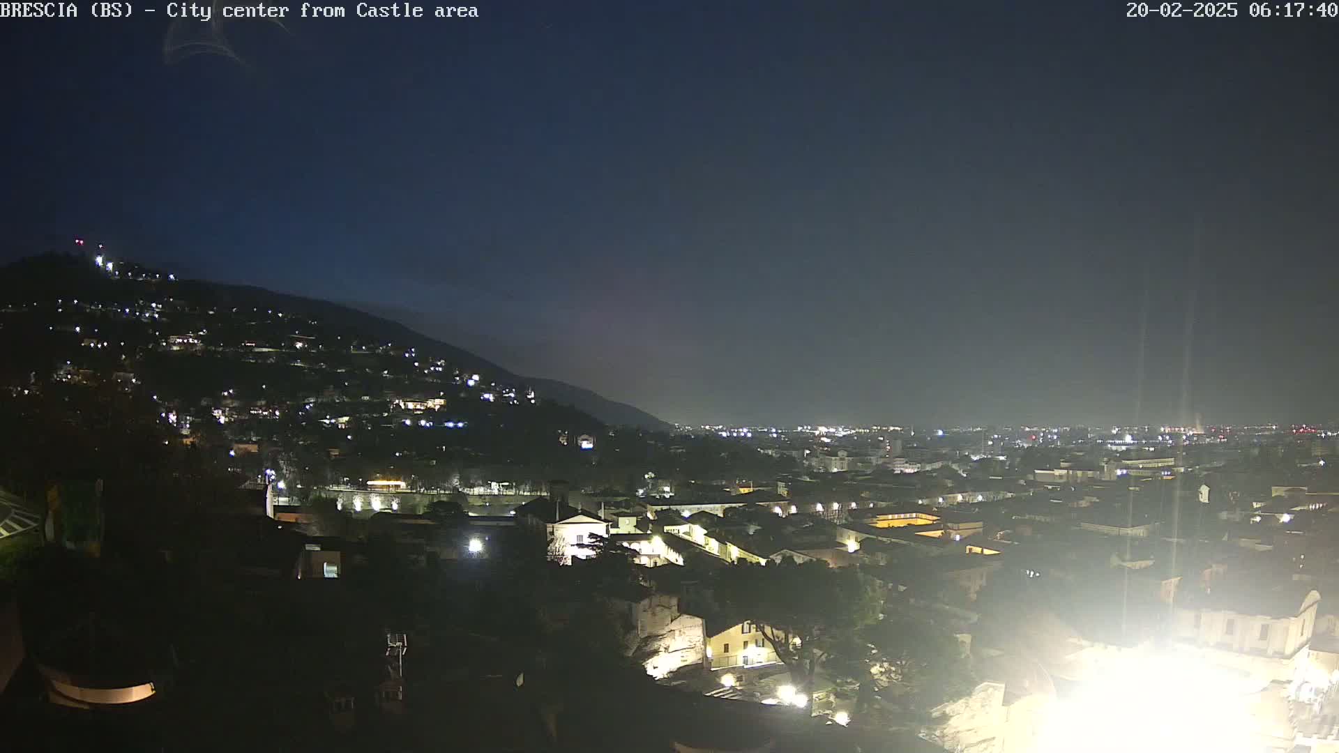 A nighttime, aerial view of a city nestled against a hillside under a dark sky.
