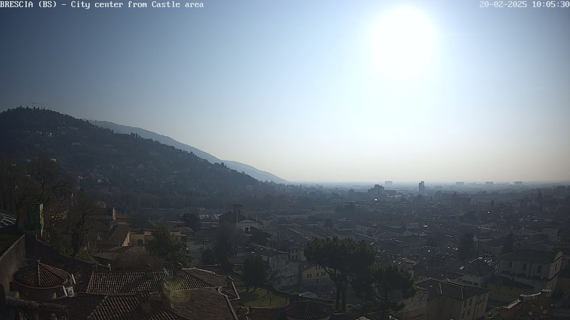 A hazy, sunny day reveals a sprawling city nestled below a mountain, viewed from a high vantage point.