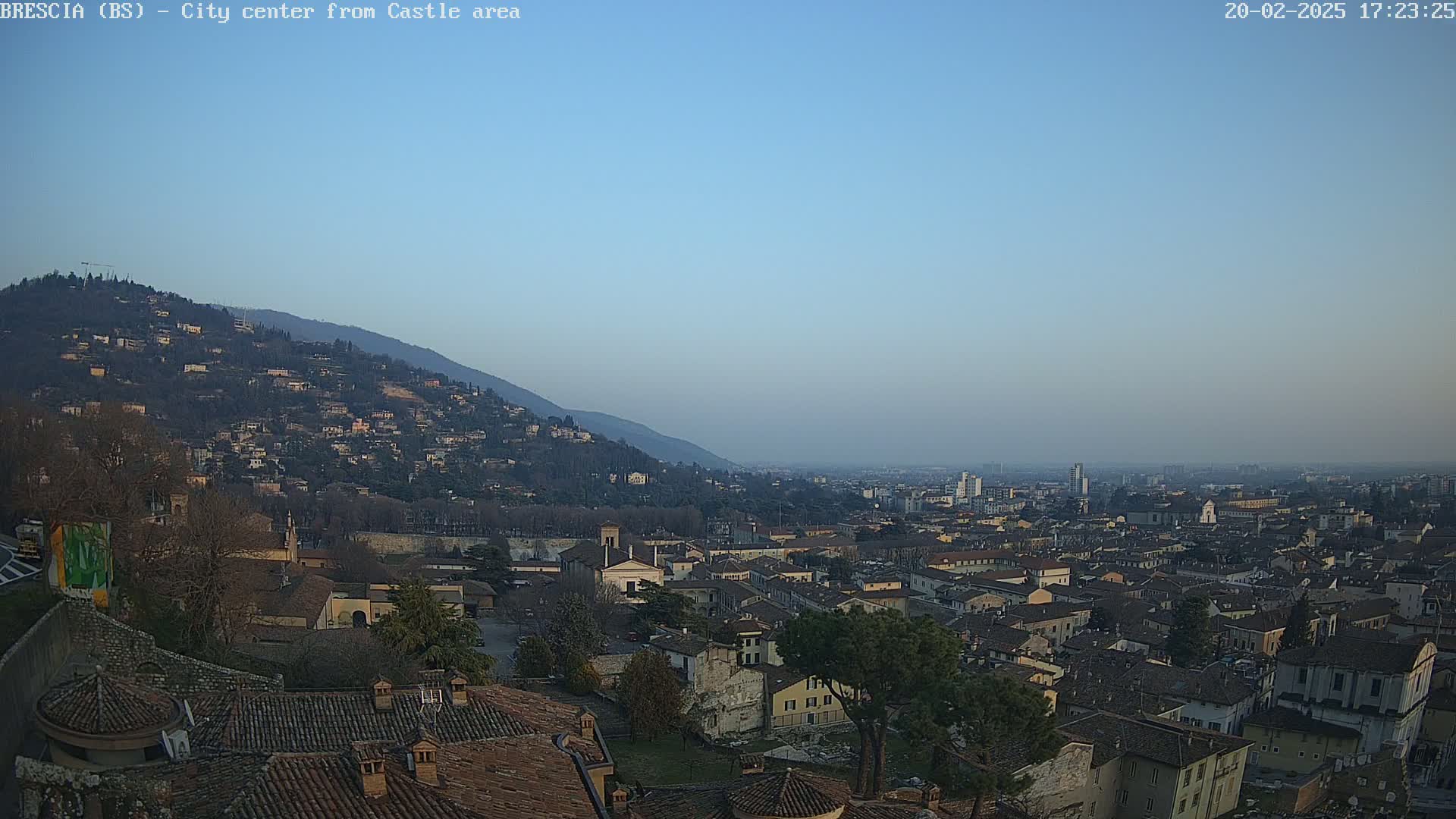 A sprawling city nestled beneath a mountain, viewed from a high vantage point under a clear, pale blue sky.