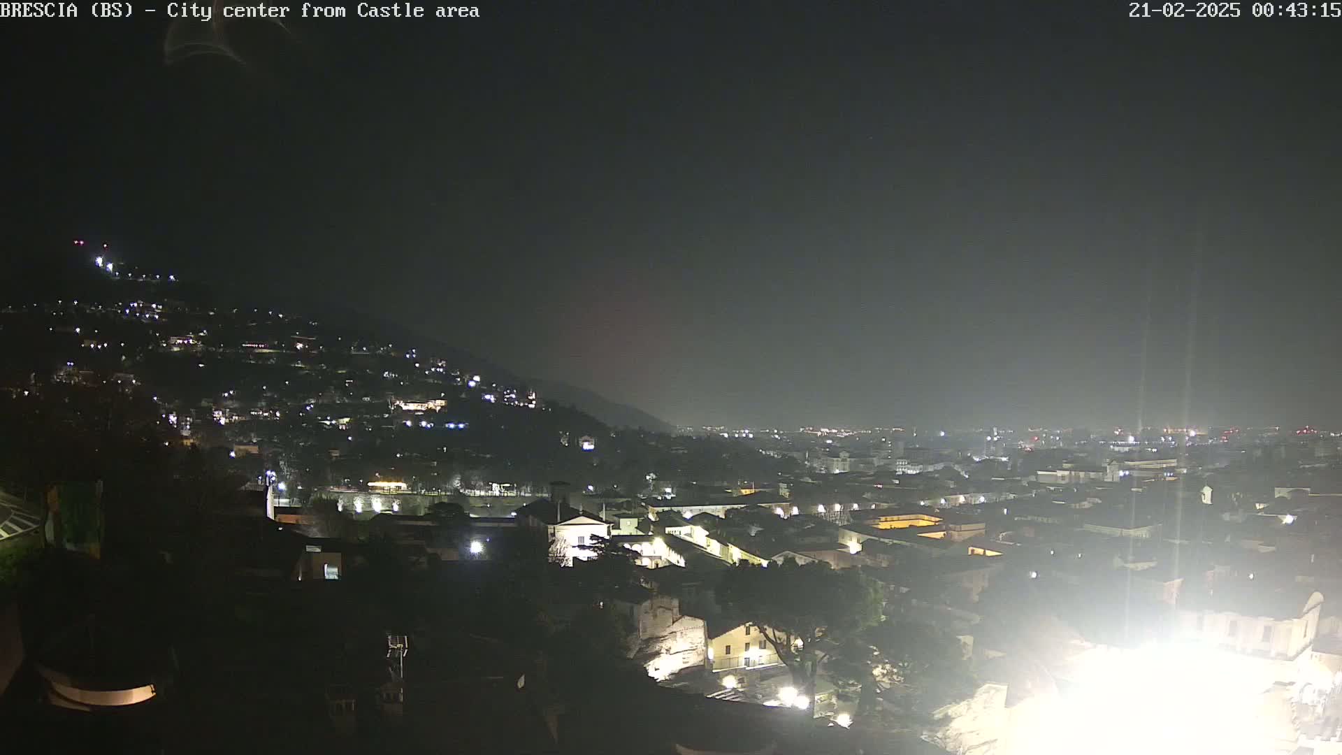 A nighttime view of a city nestled against a hill, with many lights illuminating buildings and streets under a dark, clear sky.