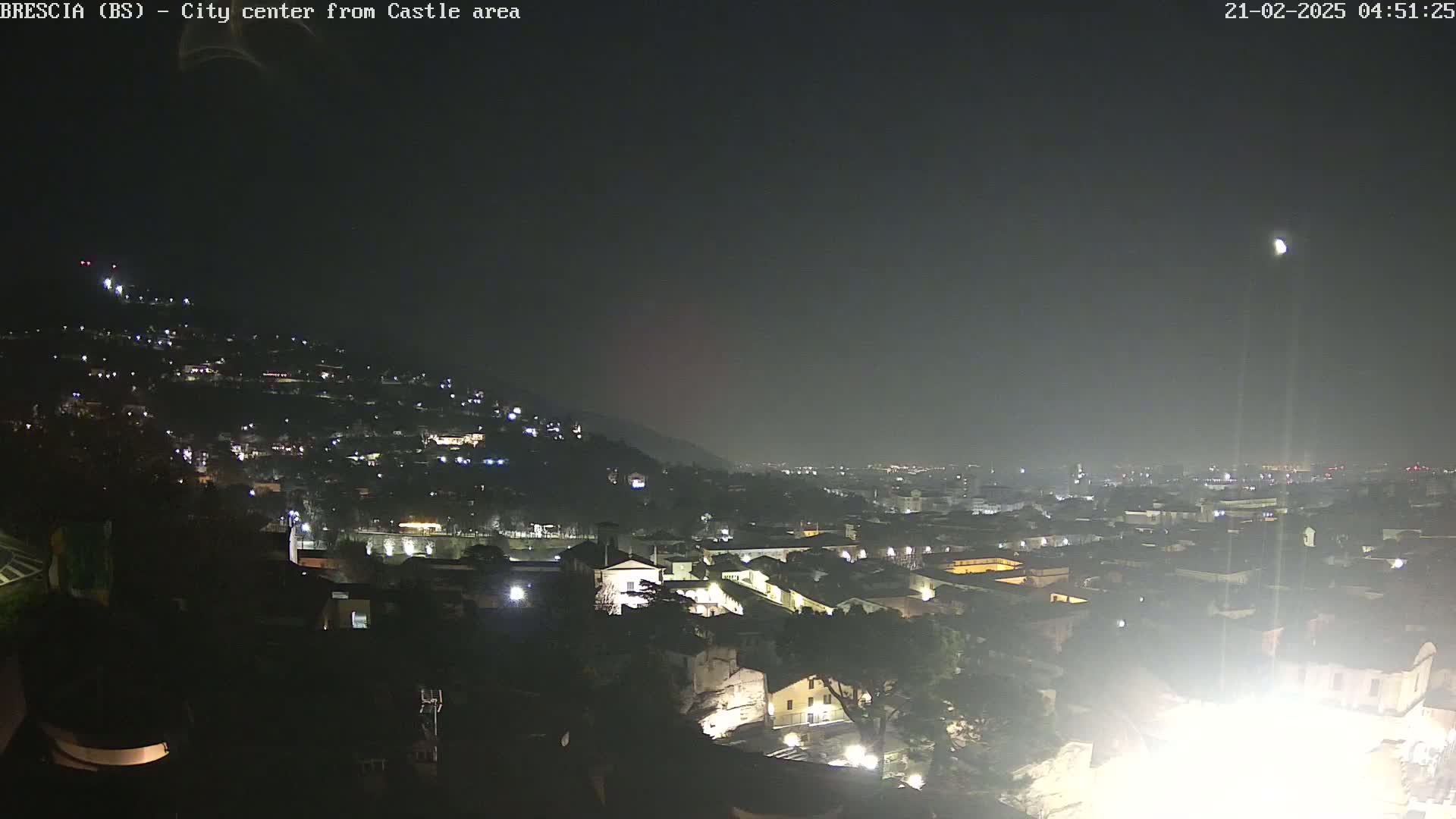 A nighttime, hazy view of a city sprawling across a hillside, illuminated by scattered lights.