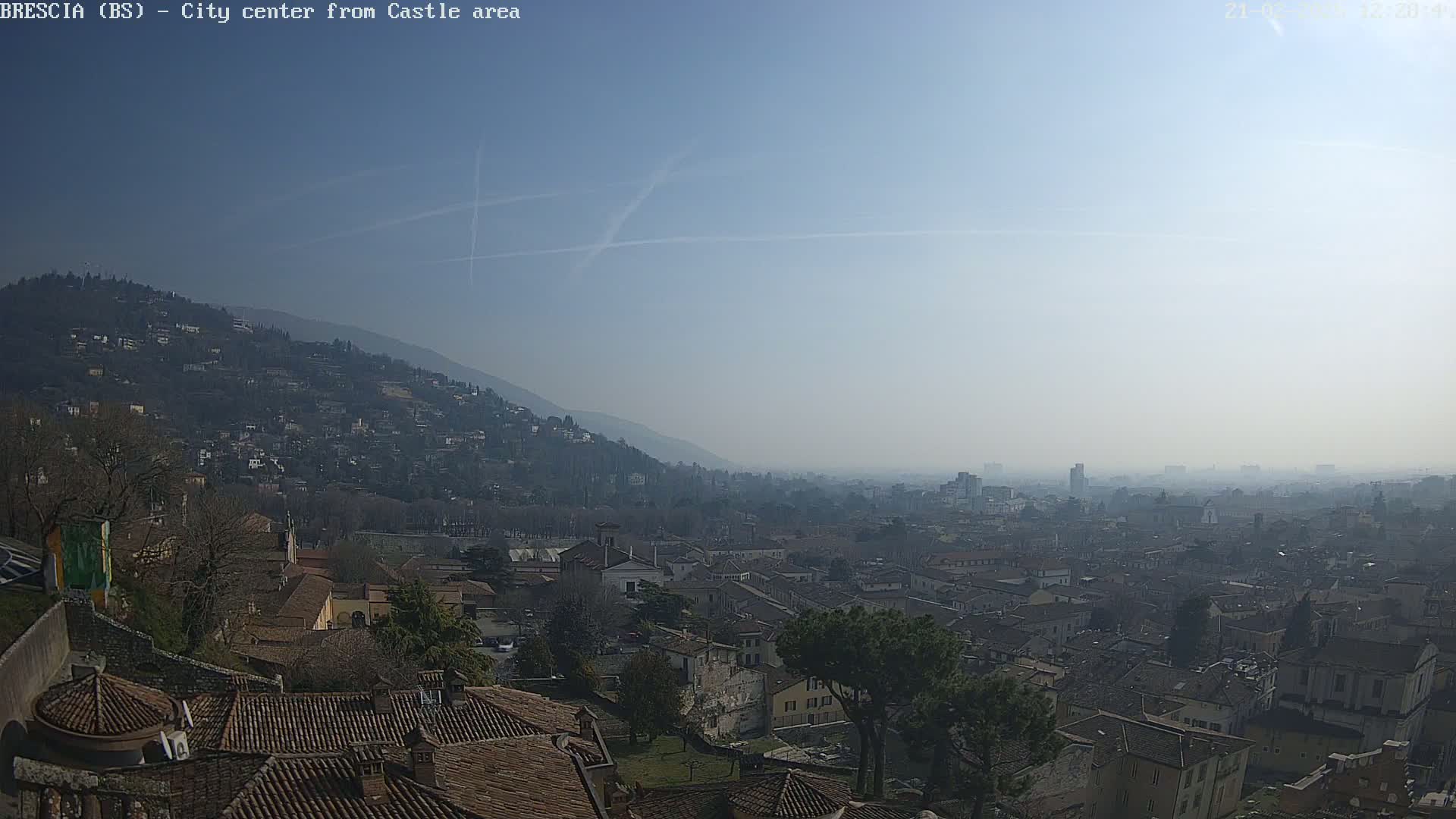 A hazy, sunny day reveals a sprawling city nestled in a valley, with a hill dotted with buildings in the background.