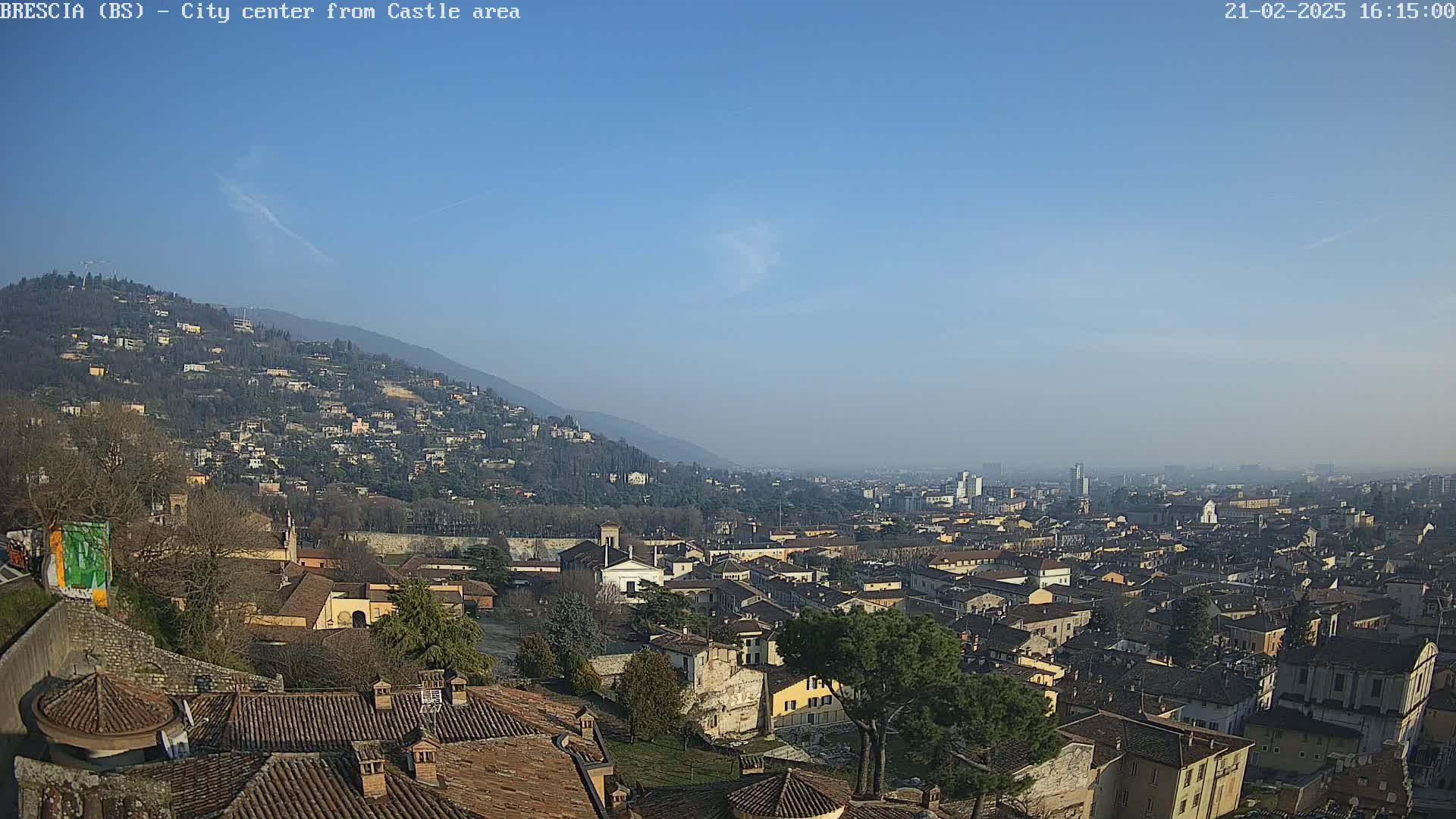 A sprawling city with terracotta rooftops nestled in a valley below a hill, under a clear blue sky.