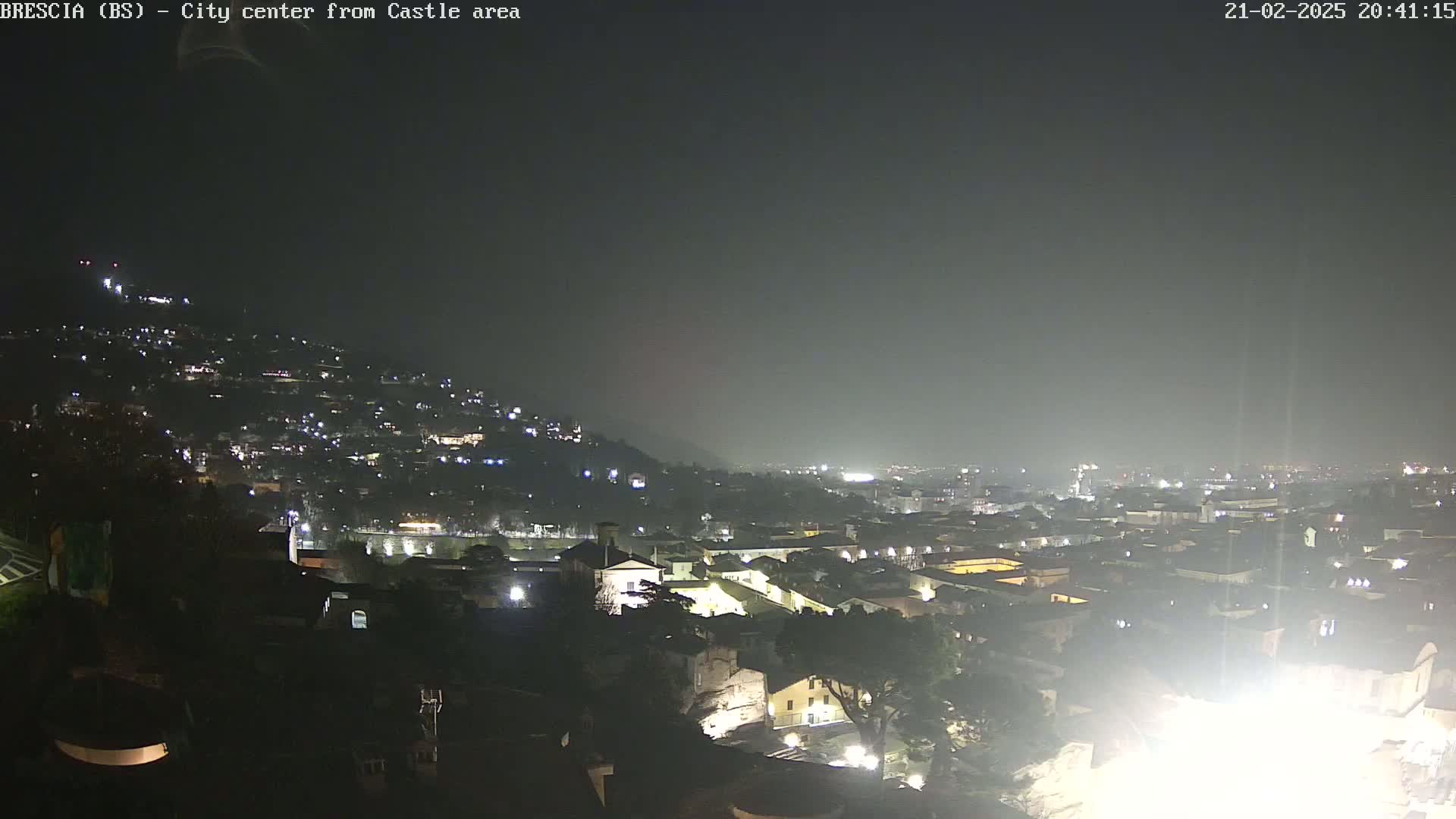 A nighttime, hazy view of a city spread across a hillside, with many lights illuminating buildings and streets.