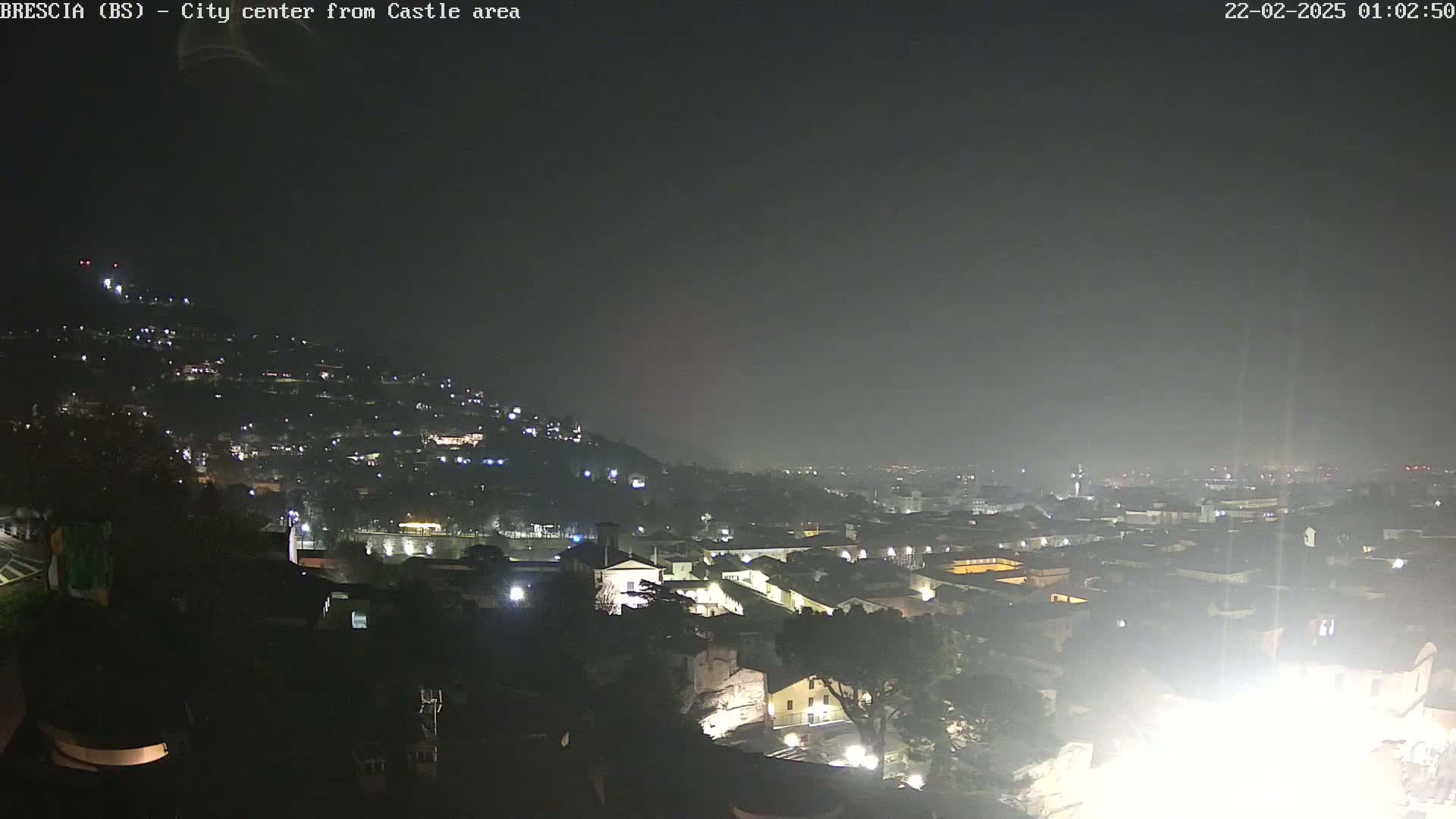 A nighttime, hazy view of a city illuminated by scattered lights, seen from a hilltop vantage point.