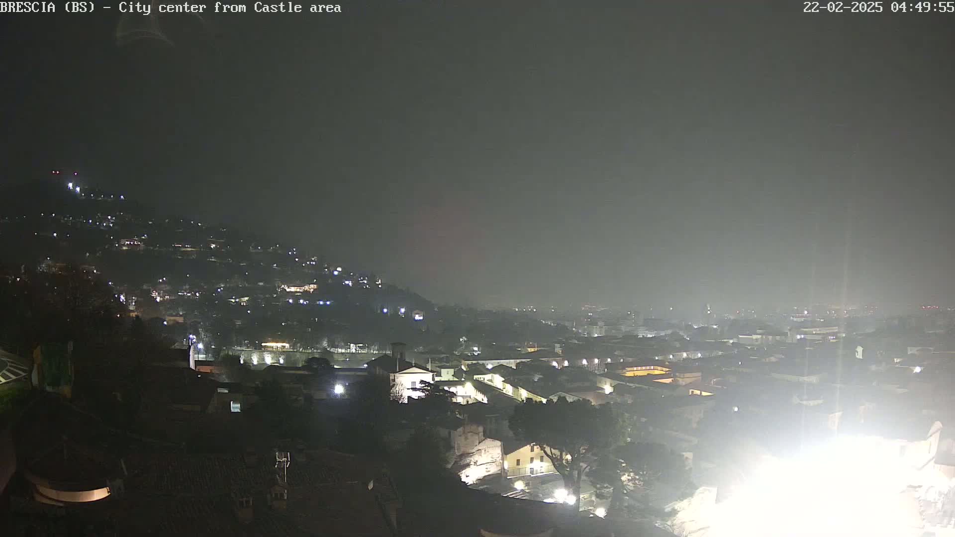 A nighttime, hazy view of a city spread across a hillside, with lights illuminating buildings and streets.