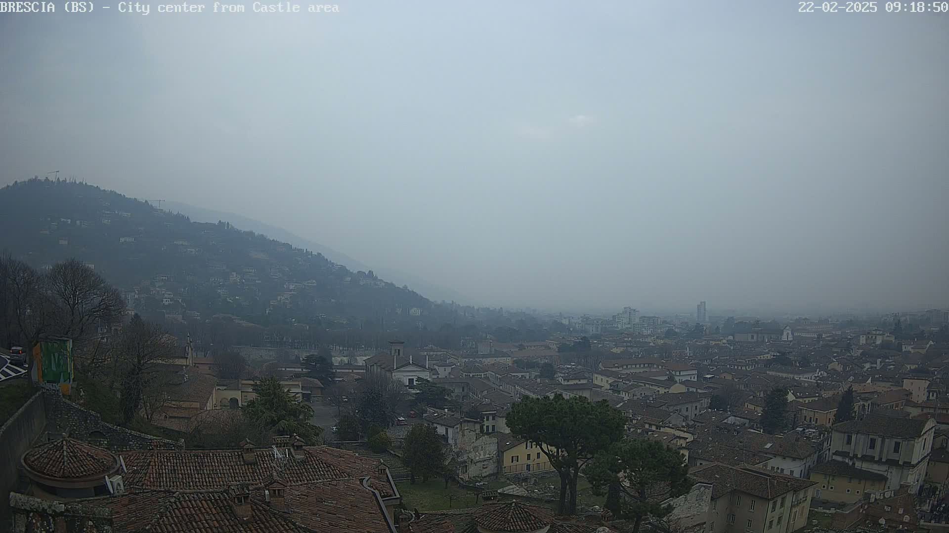 A hazy, overcast view of a city nestled in a valley, with a hill rising in the background.