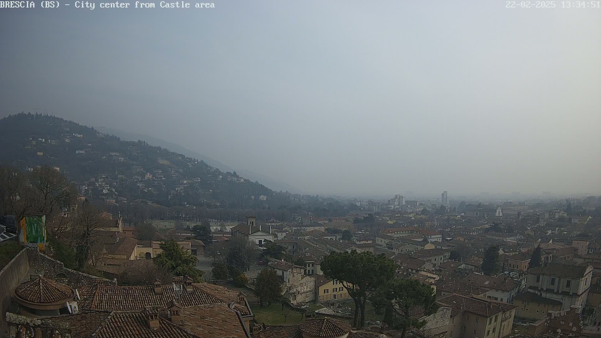 A hazy view of a city nestled in a valley, seen from a hilltop with many buildings and terracotta roofs.