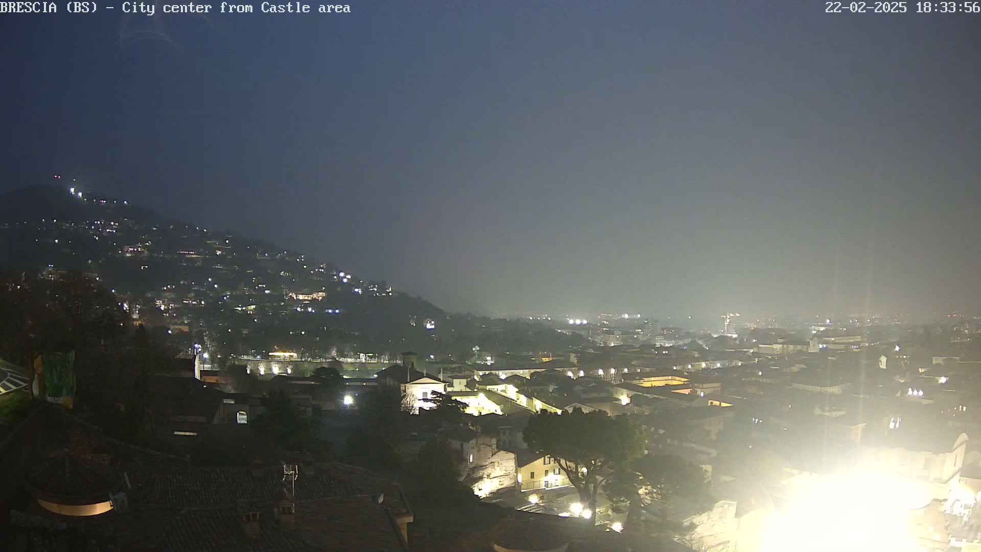 A nighttime, hazy view of a city sprawling across a hillside, with numerous lights illuminating buildings and streets.