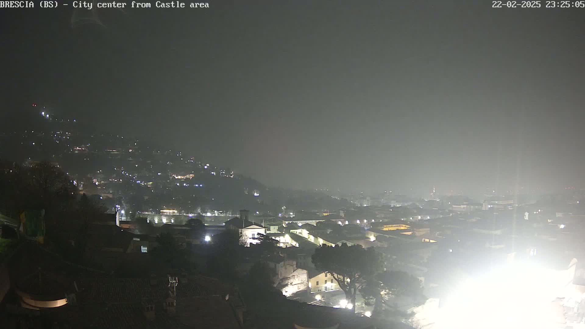 A nighttime view of a city shrouded in fog, showing numerous lights scattered across the cityscape and hillsides.