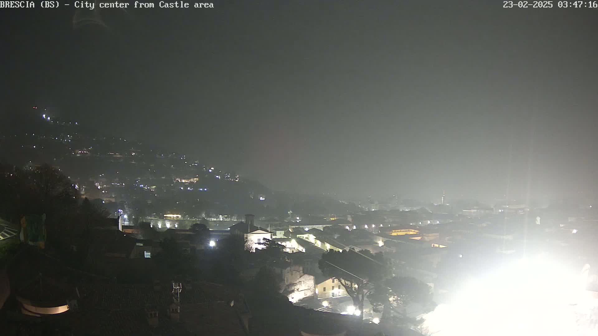 A nighttime, foggy view of a city sprawling across a hill, illuminated by scattered lights.