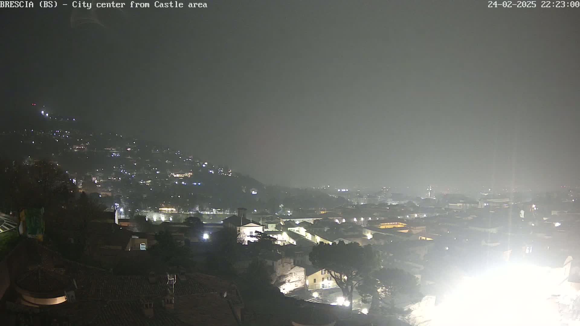 A nighttime view of a city shrouded in fog, with numerous lights illuminating buildings and streets below.
