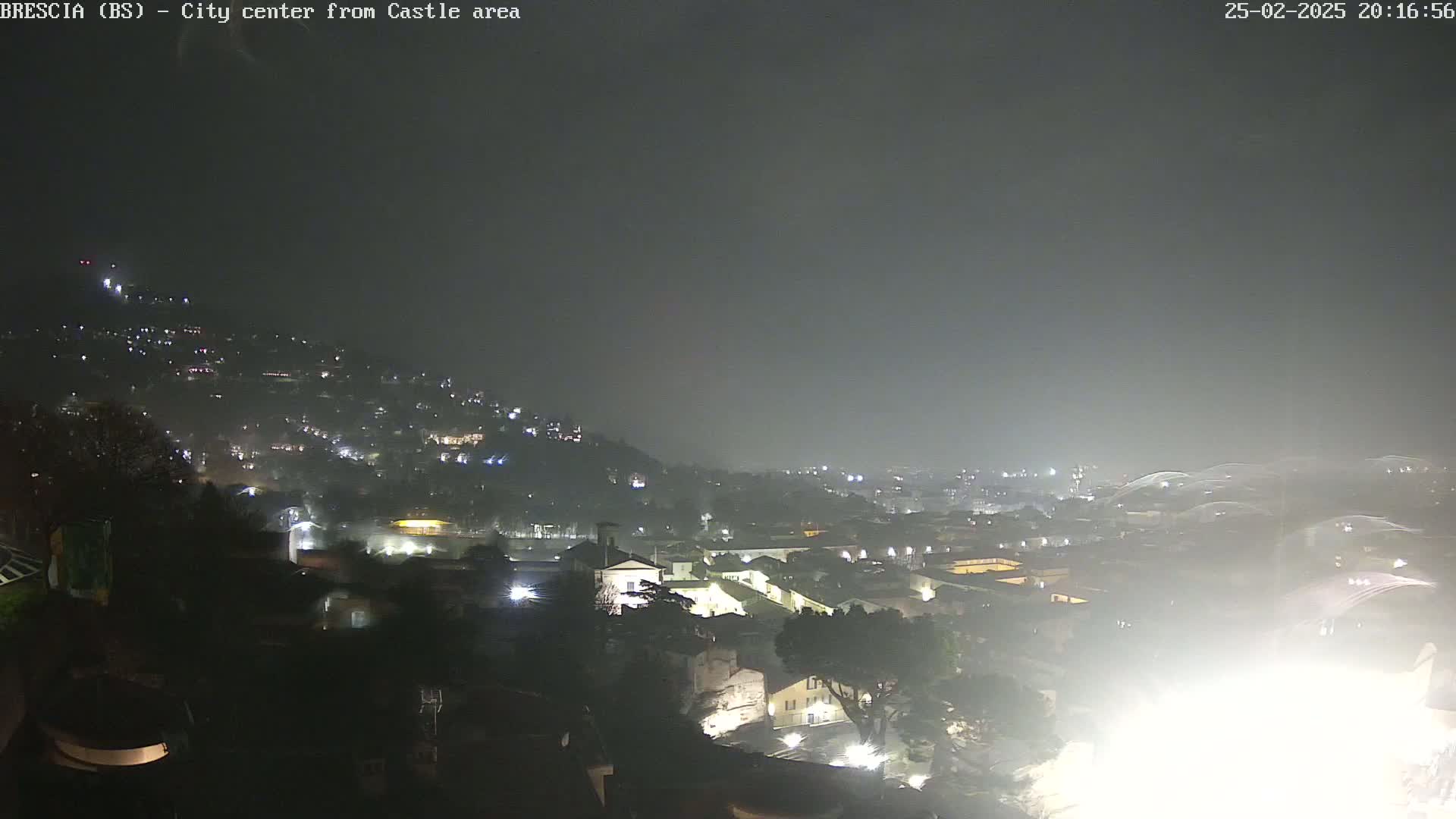 A nighttime, hazy view of a city sprawling across a hill, illuminated by scattered lights.