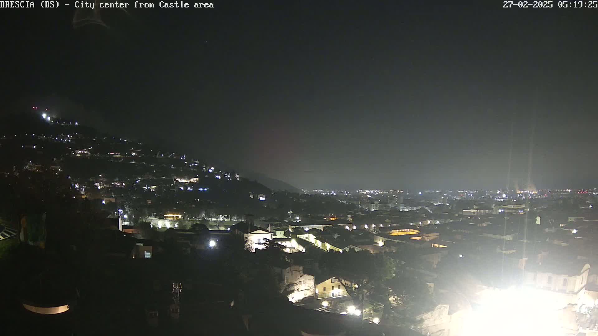 A nighttime view of a city nestled in a valley, illuminated by scattered lights under a dark, clear sky.