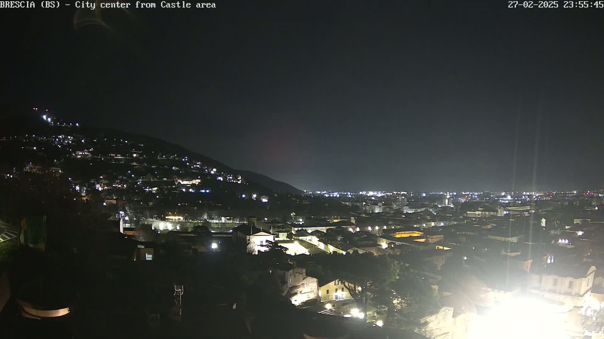 A nighttime, high-angle view of a city sprawling across a hillside, illuminated by numerous lights.