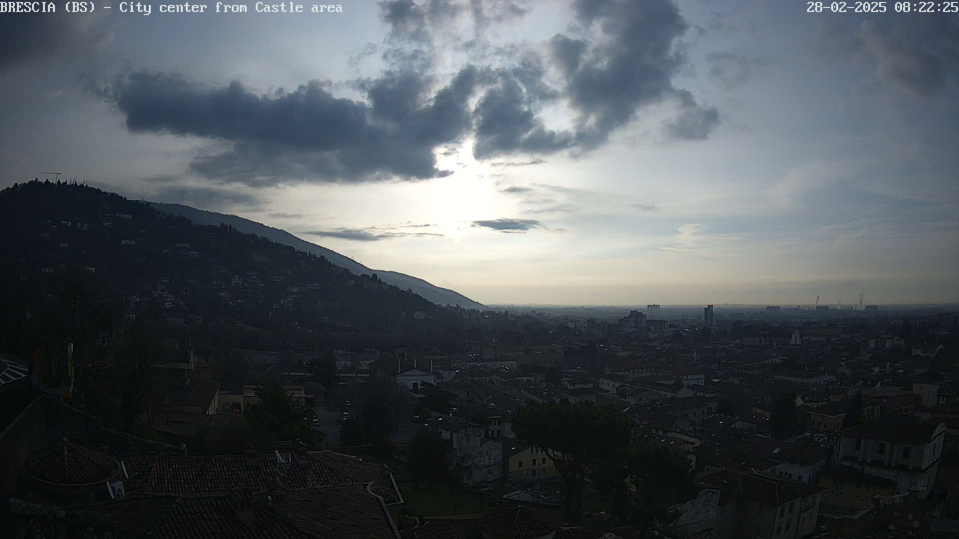 A sun-dappled city sprawls below a hill, under a partly cloudy sky.