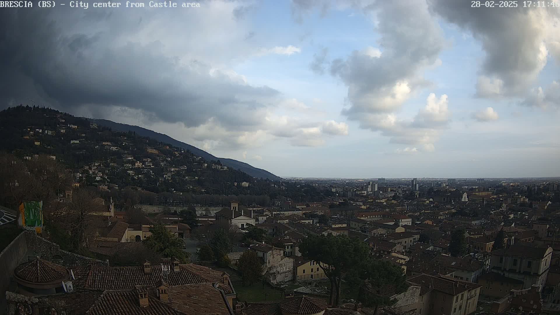 A sprawling city nestled at the base of a hill under a partly cloudy sky.