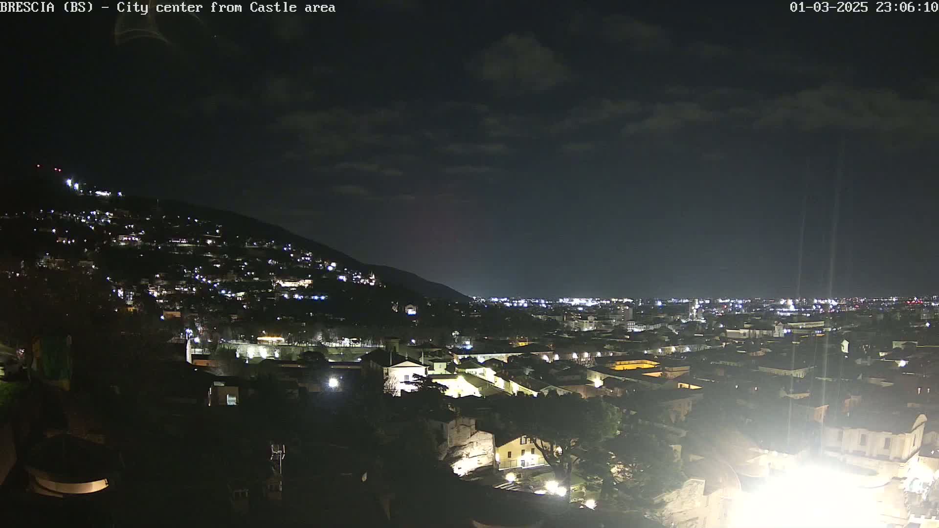 A nighttime view of a city nestled against a hill, under a partly cloudy sky.