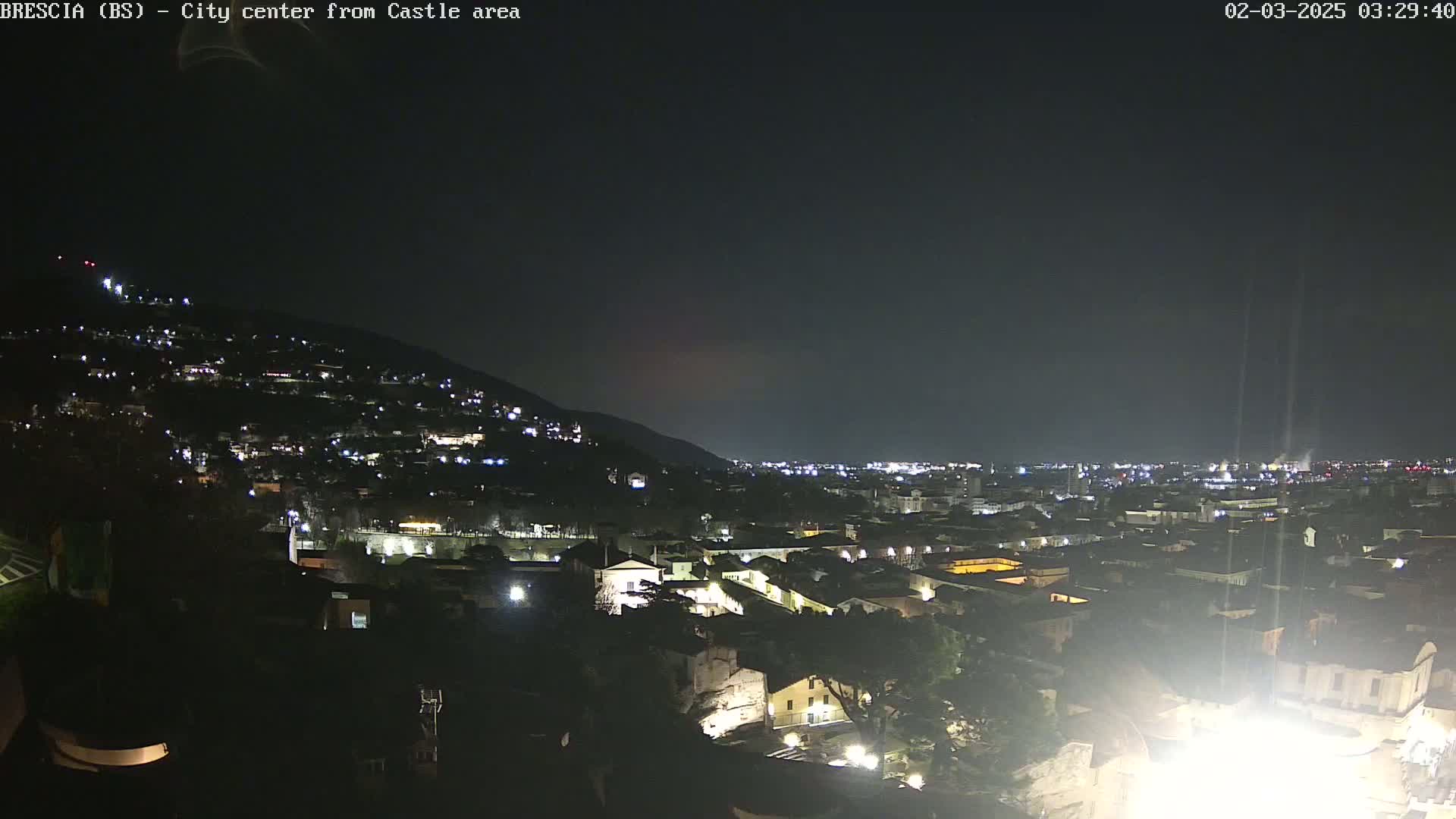 A nighttime, long shot of a city nestled against a hill, illuminated by scattered lights under a dark, clear sky.