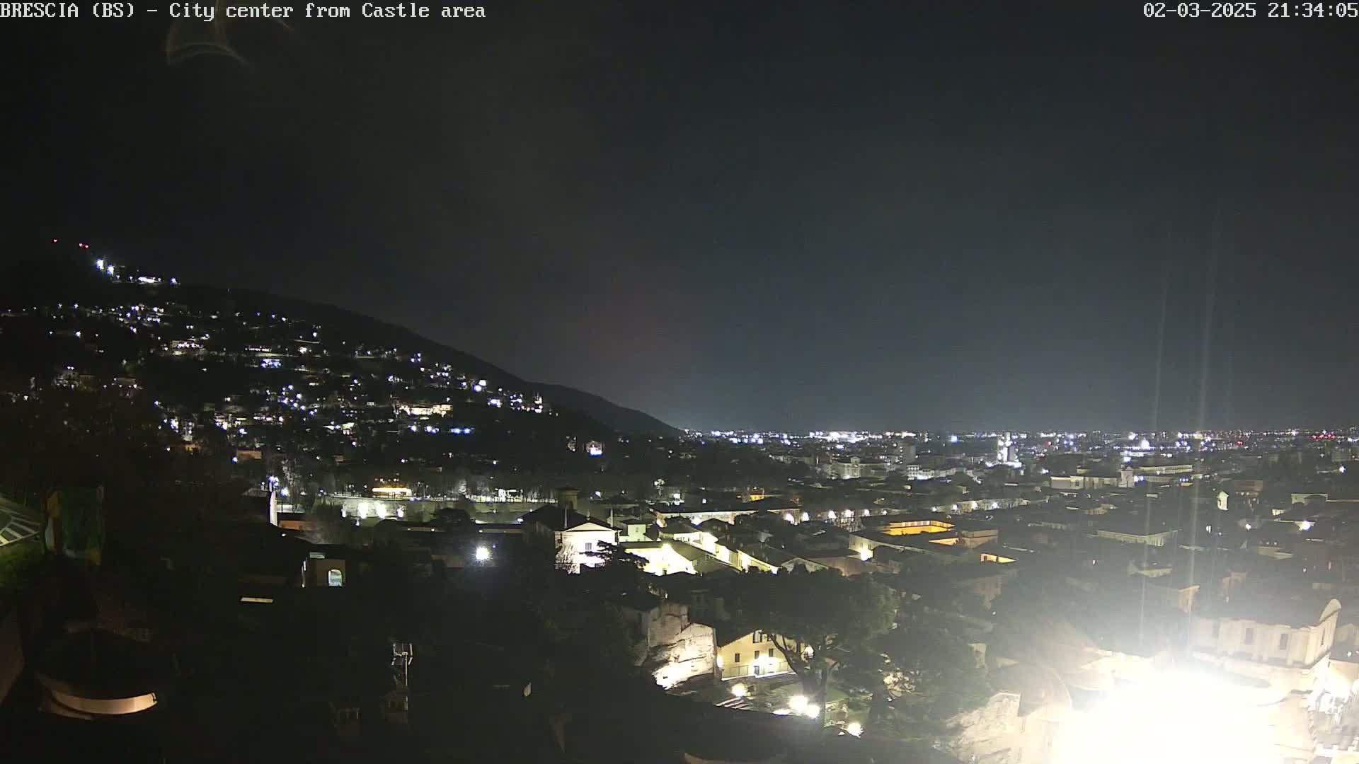 A nighttime view of a city nestled against a hillside, illuminated by numerous lights under a clear, dark sky.