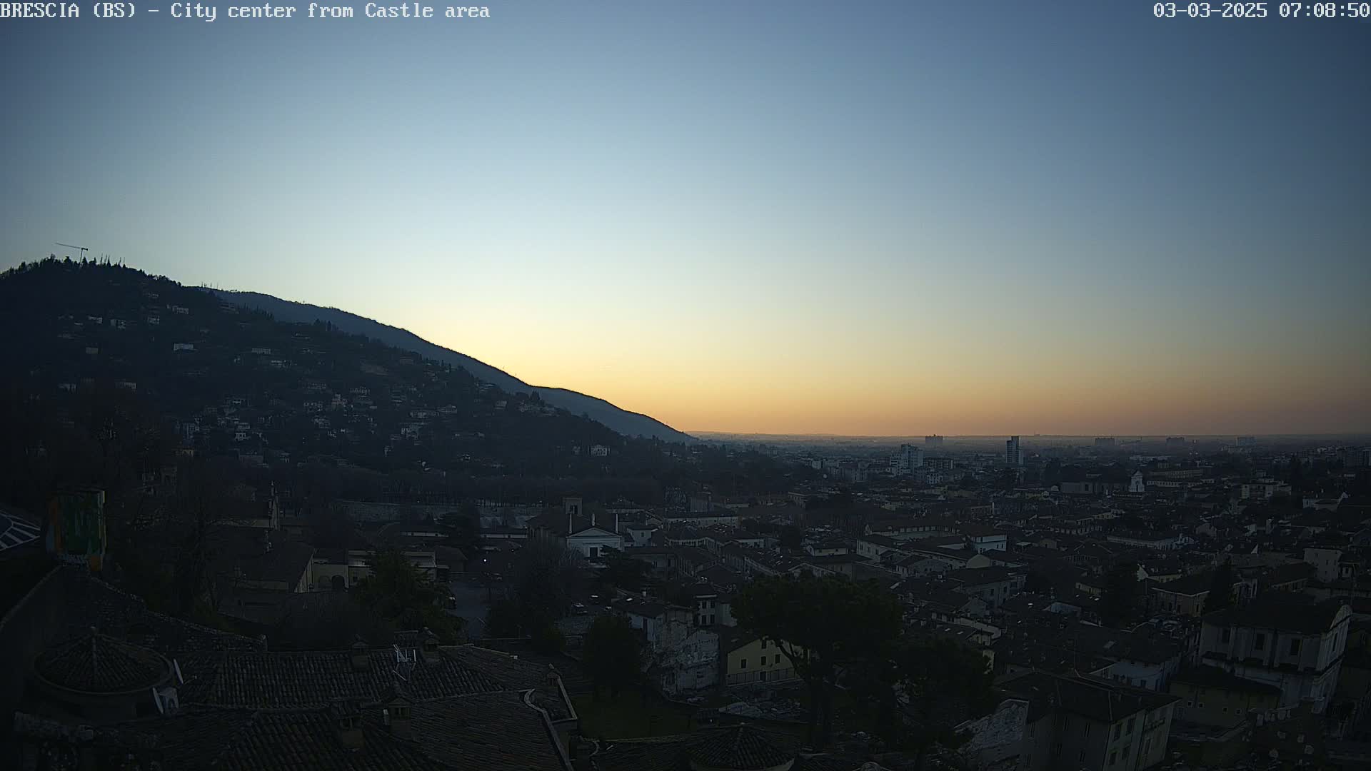A city at sunrise, nestled at the base of a hill, under a clear, twilight sky.