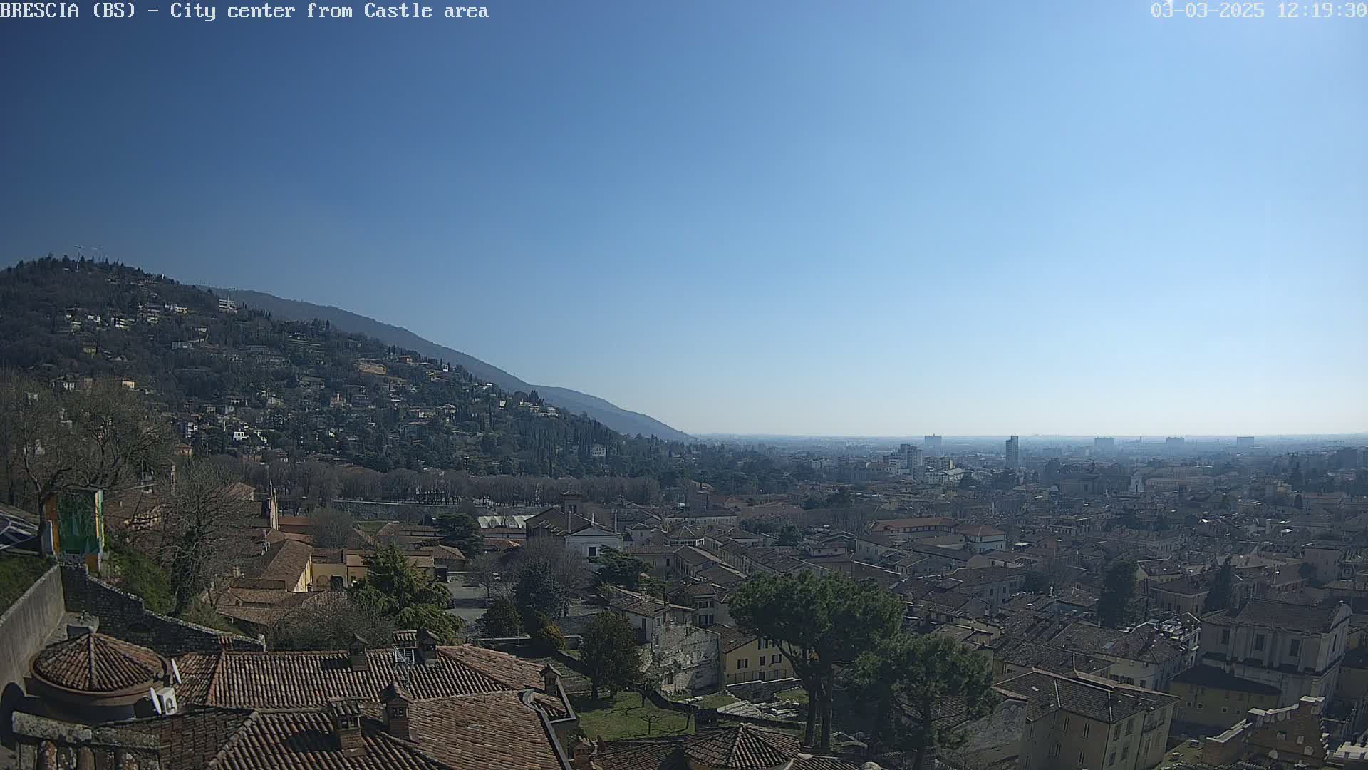 A sprawling city with red-tiled roofs nestled against a mountainside under a clear blue sky.