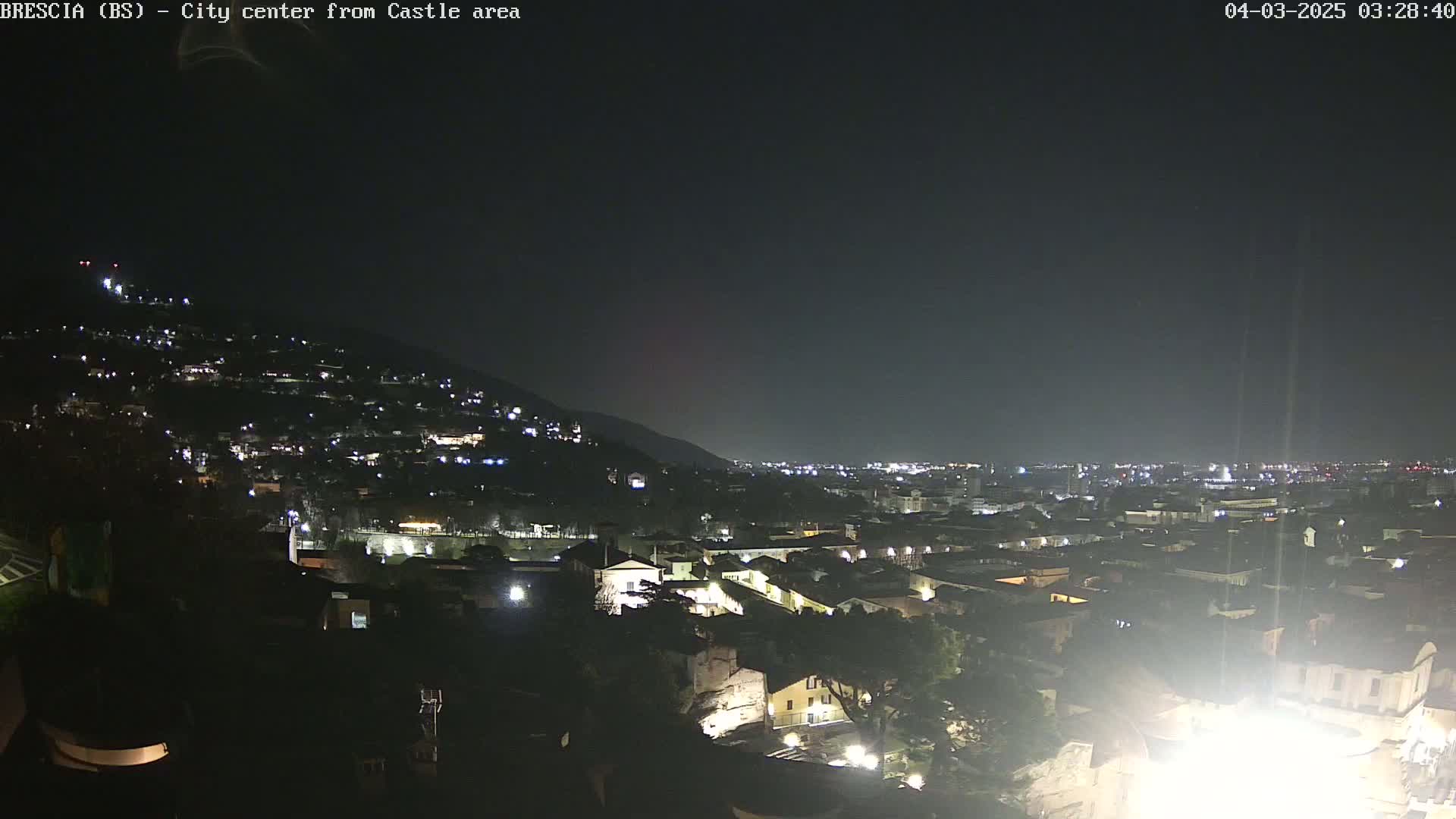 A nighttime view of a city nestled against a hill, illuminated by scattered lights under a dark sky.