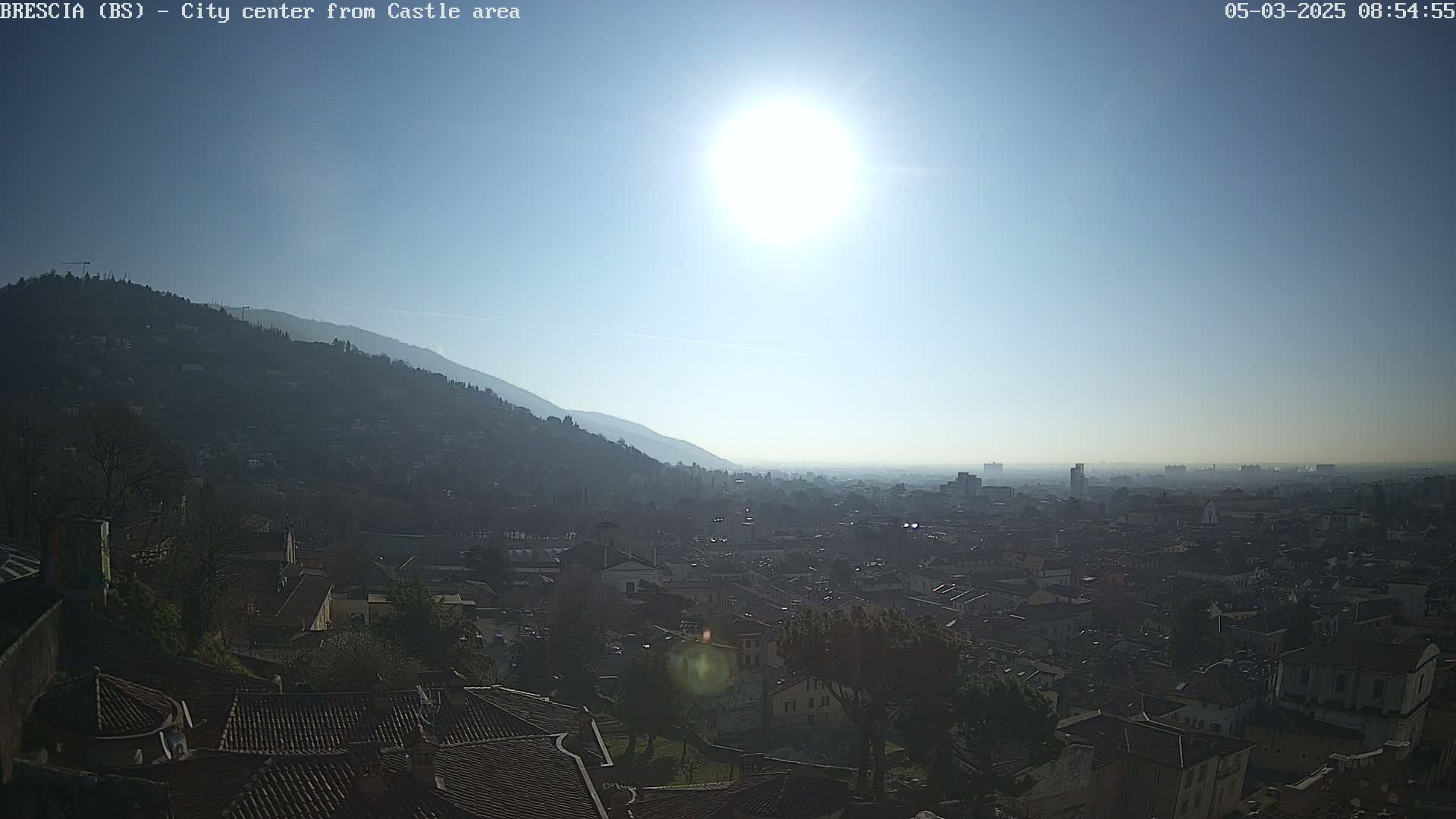 A sunny day reveals a sprawling city nestled beneath a hill, viewed from a higher vantage point.