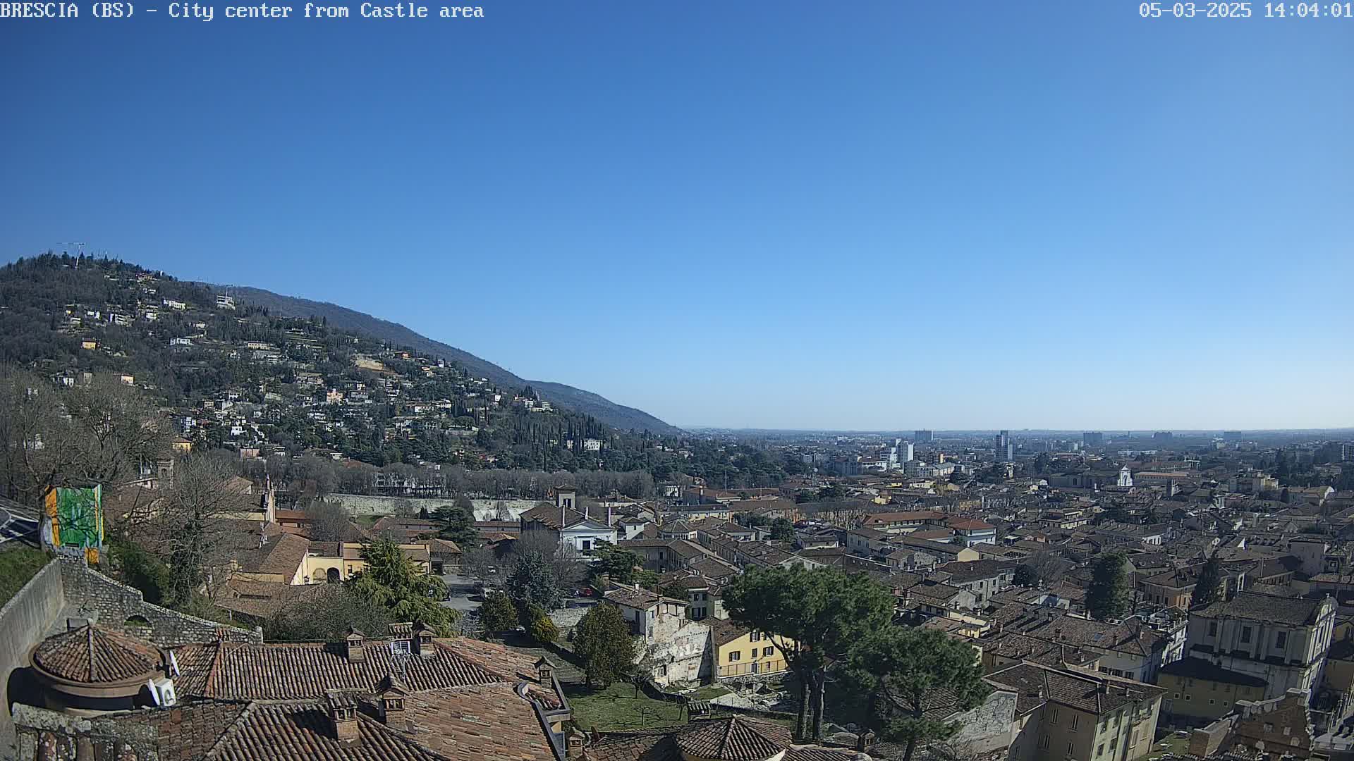 A sprawling city with red-tiled roofs nestles against a hillside under a clear blue sky.