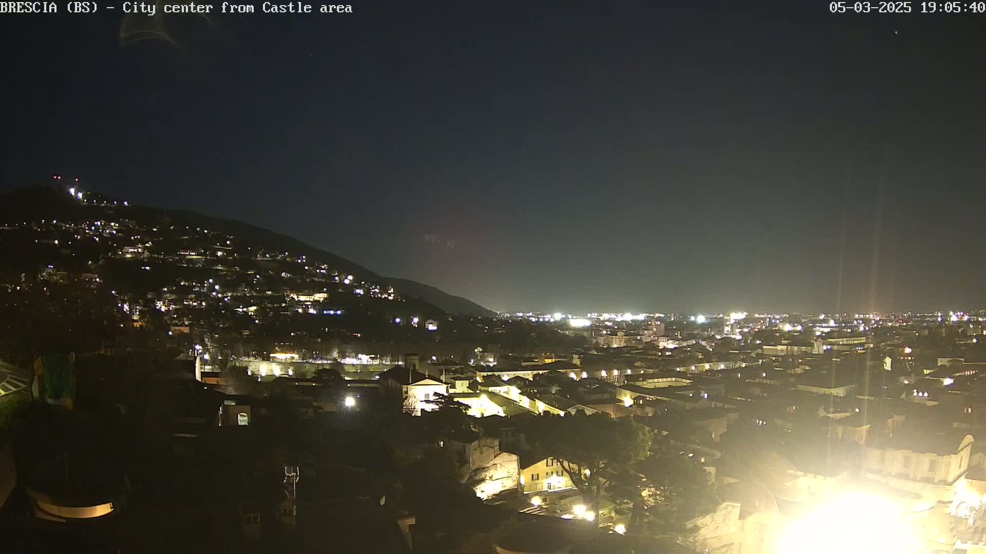 A nighttime view of a city illuminated by lights, nestled against a hill under a clear, dark sky.