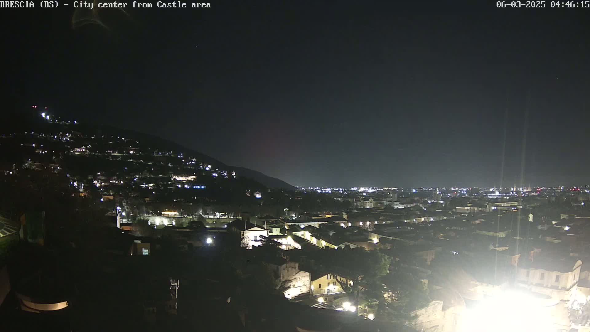 A nighttime view of a city nestled against a hill, with scattered lights illuminating buildings and streets under a clear, dark sky.